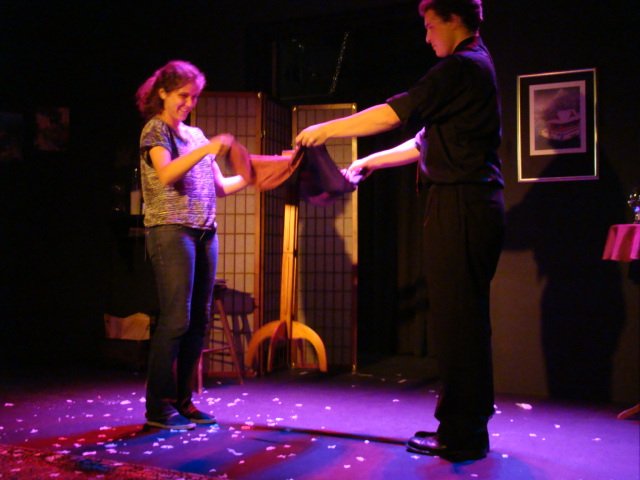 Evan and an audience member stand on stage. A wooden table floats between them