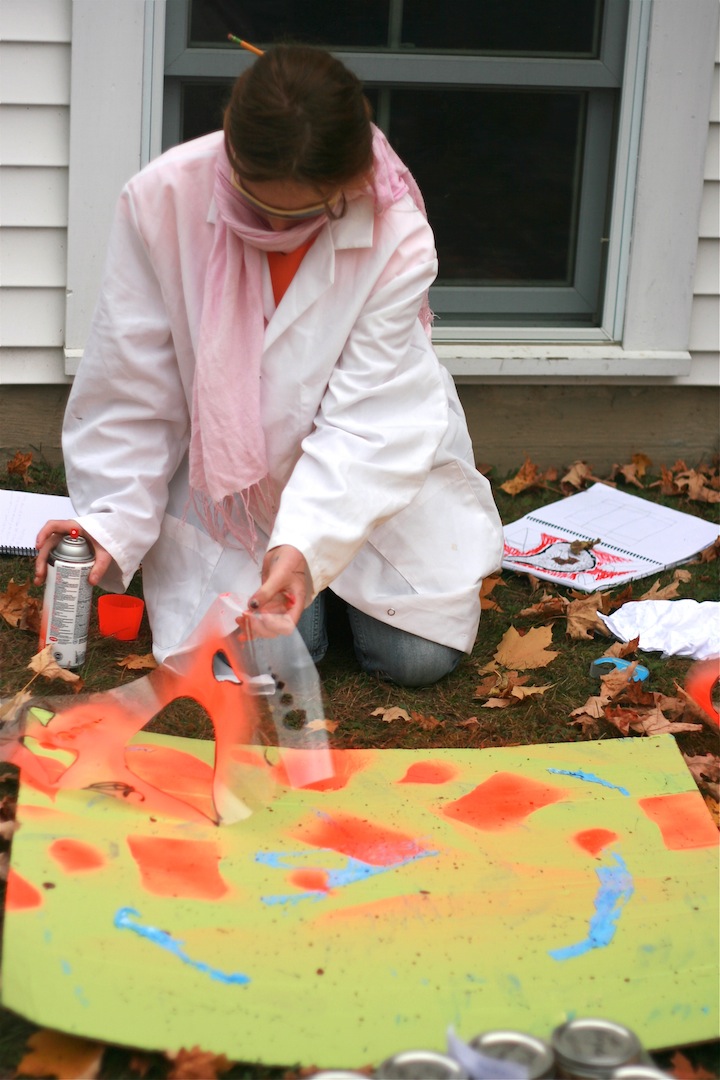 Using bright colors on cardboard the young girl with long hair paints using spray paint.