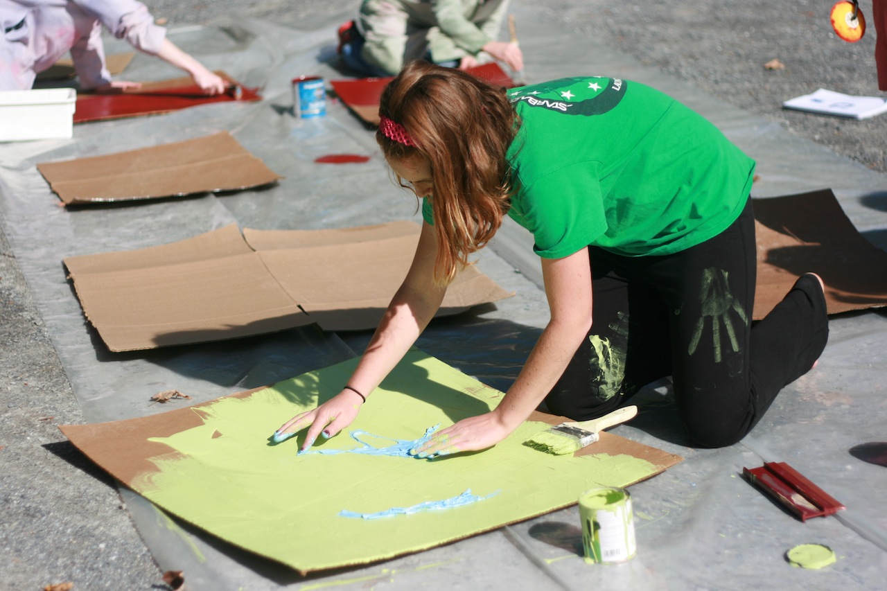 A young person with long hair painting on a yellow cardboard.