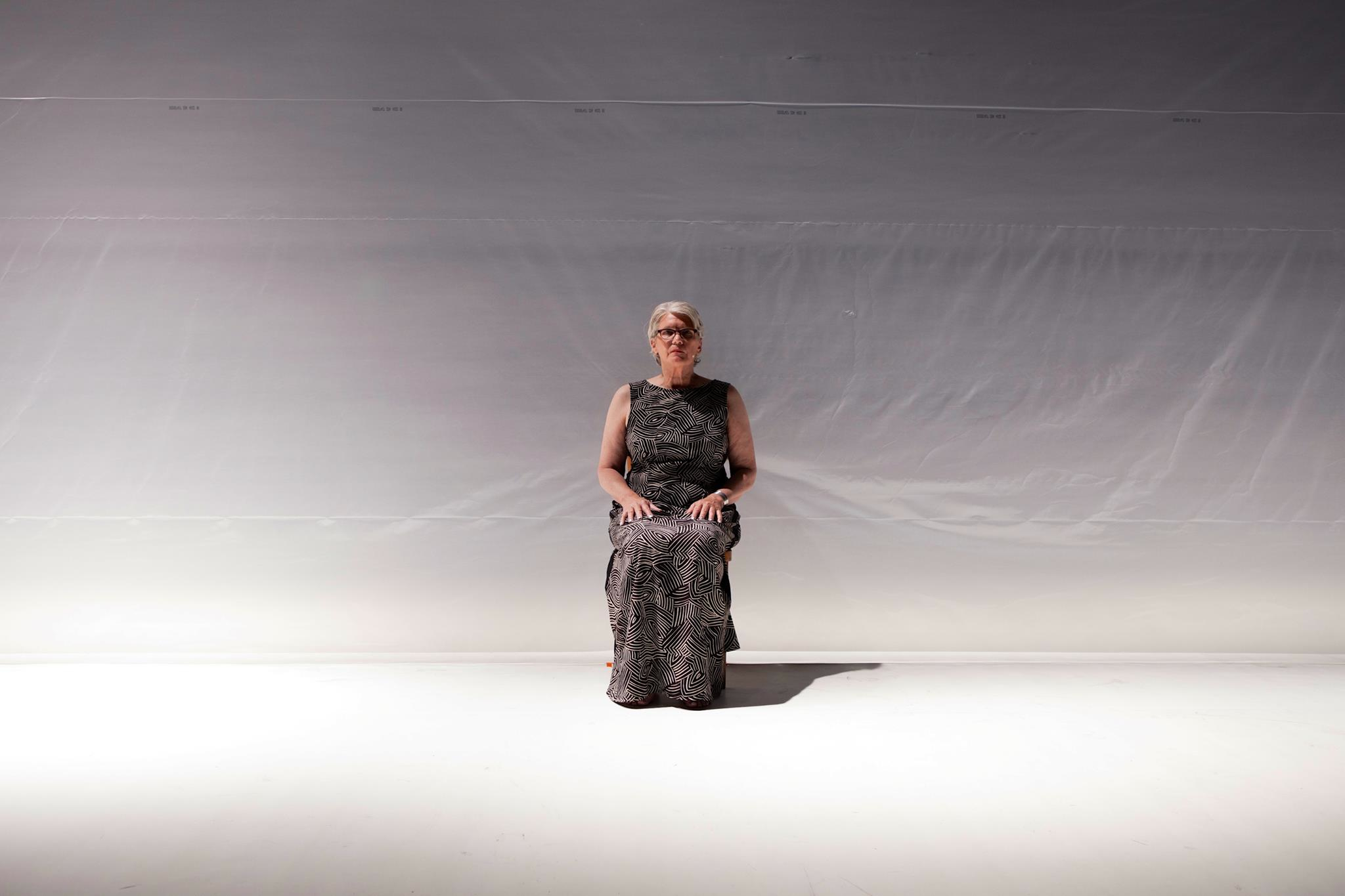 Janice Perry a.k.a. Gal seated in front of an opaque white  curtain