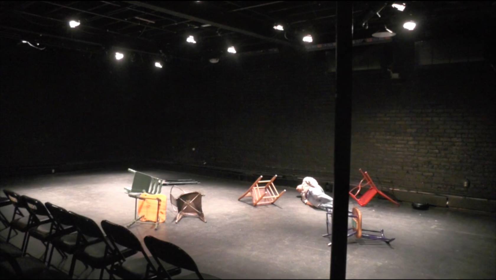 man lying down amongst fallen chairs