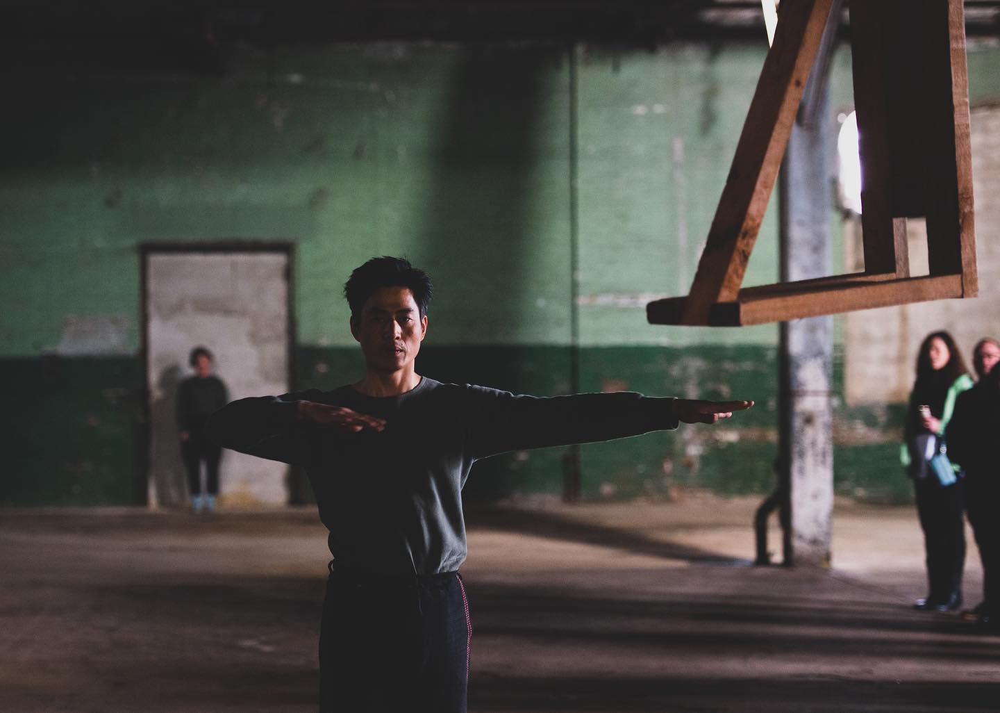 dancer Jungwoong Kim extends his arm during a performance of "JUNKSPACE" in Philadelphia, with a wooden bench hanging from the ceiling next to him