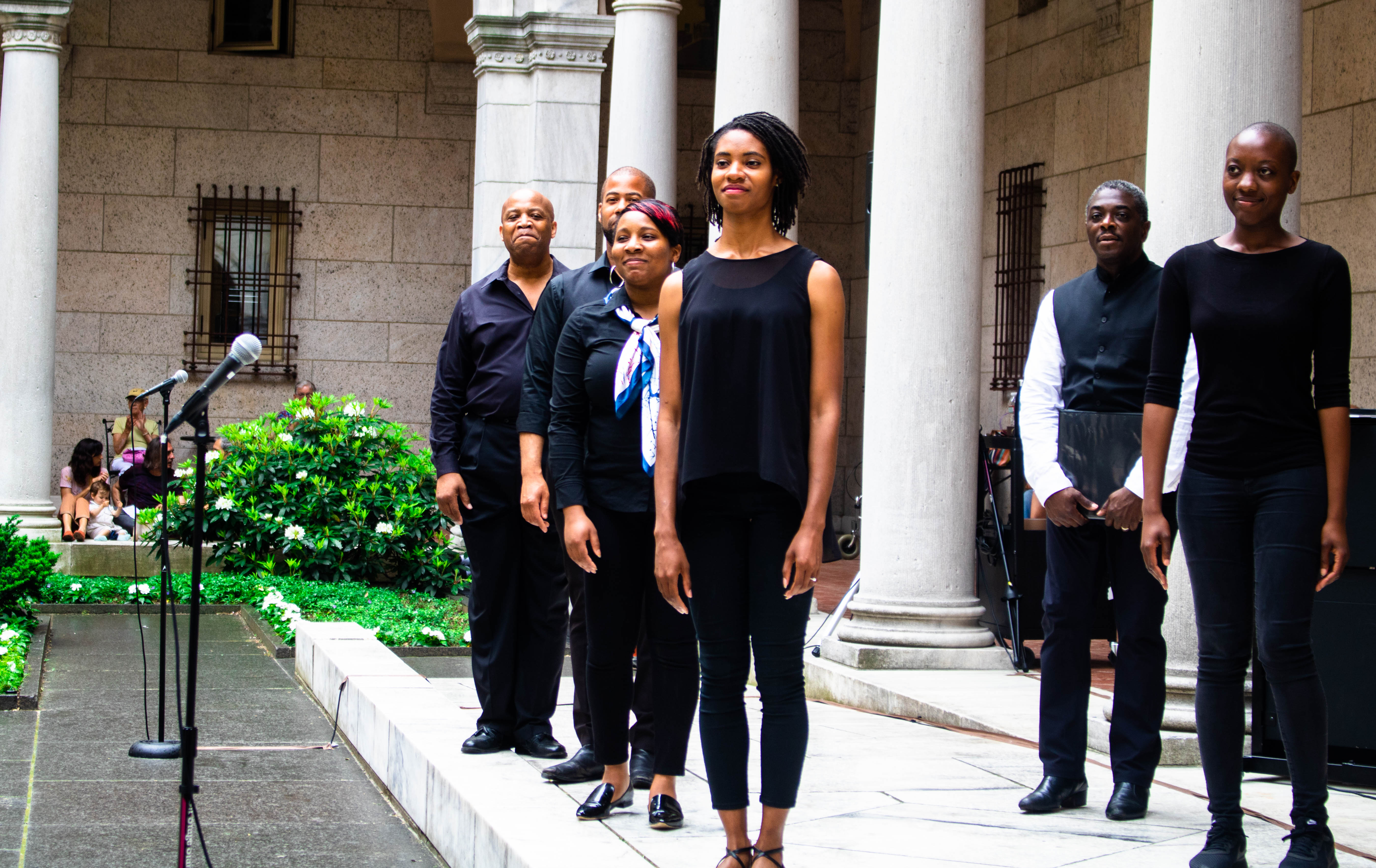 A group of Black male and female performers proudly standing in a line smiliing.