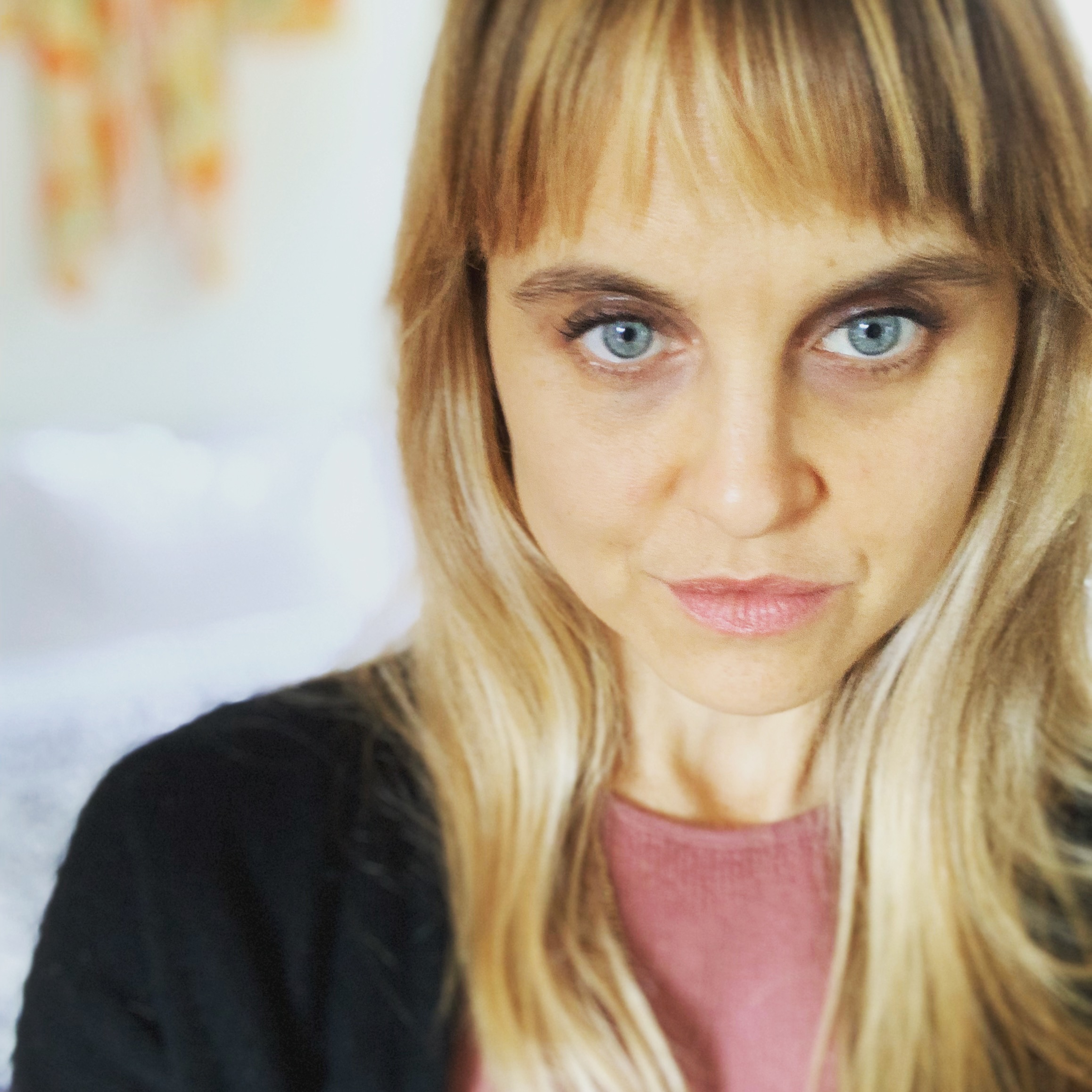 a face is framed towards the right, light eyes and hair, pink shirt and black sweater. Small smile.