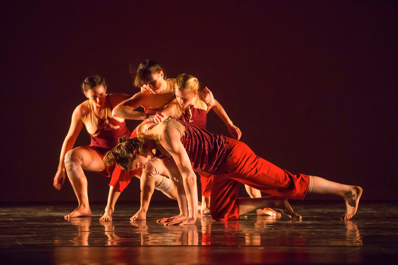 4 dancers in contact with each other in a low level position wearing red