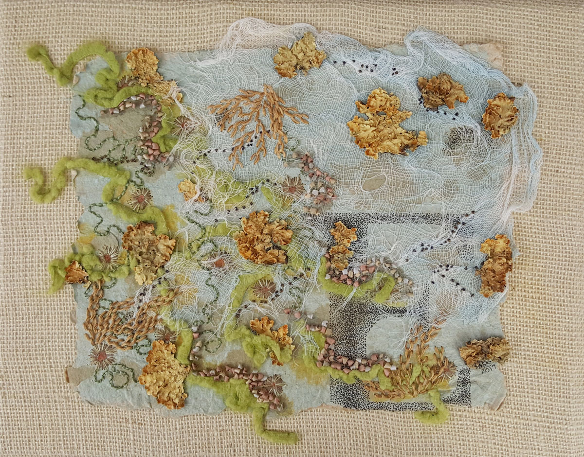 A collage of light blue paper with textured embroidery in golds and greens