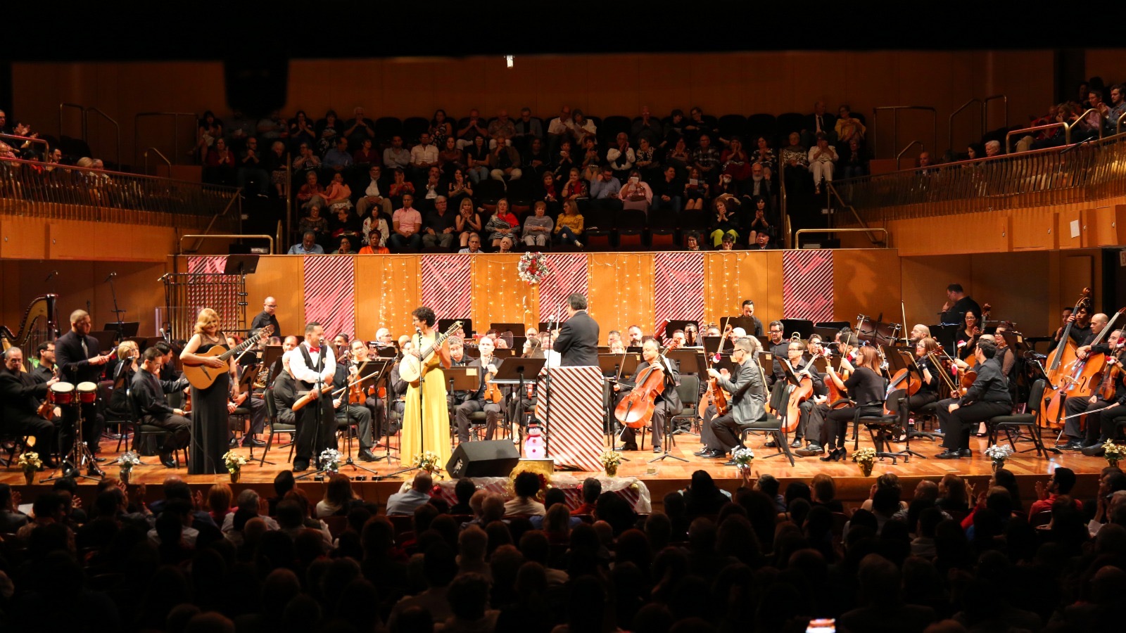 Image shows cuatrista Fabiola Méndez standing in front of the Puerto Rican Symphony Orchestra at Symphony Hall in Santurce, PR
