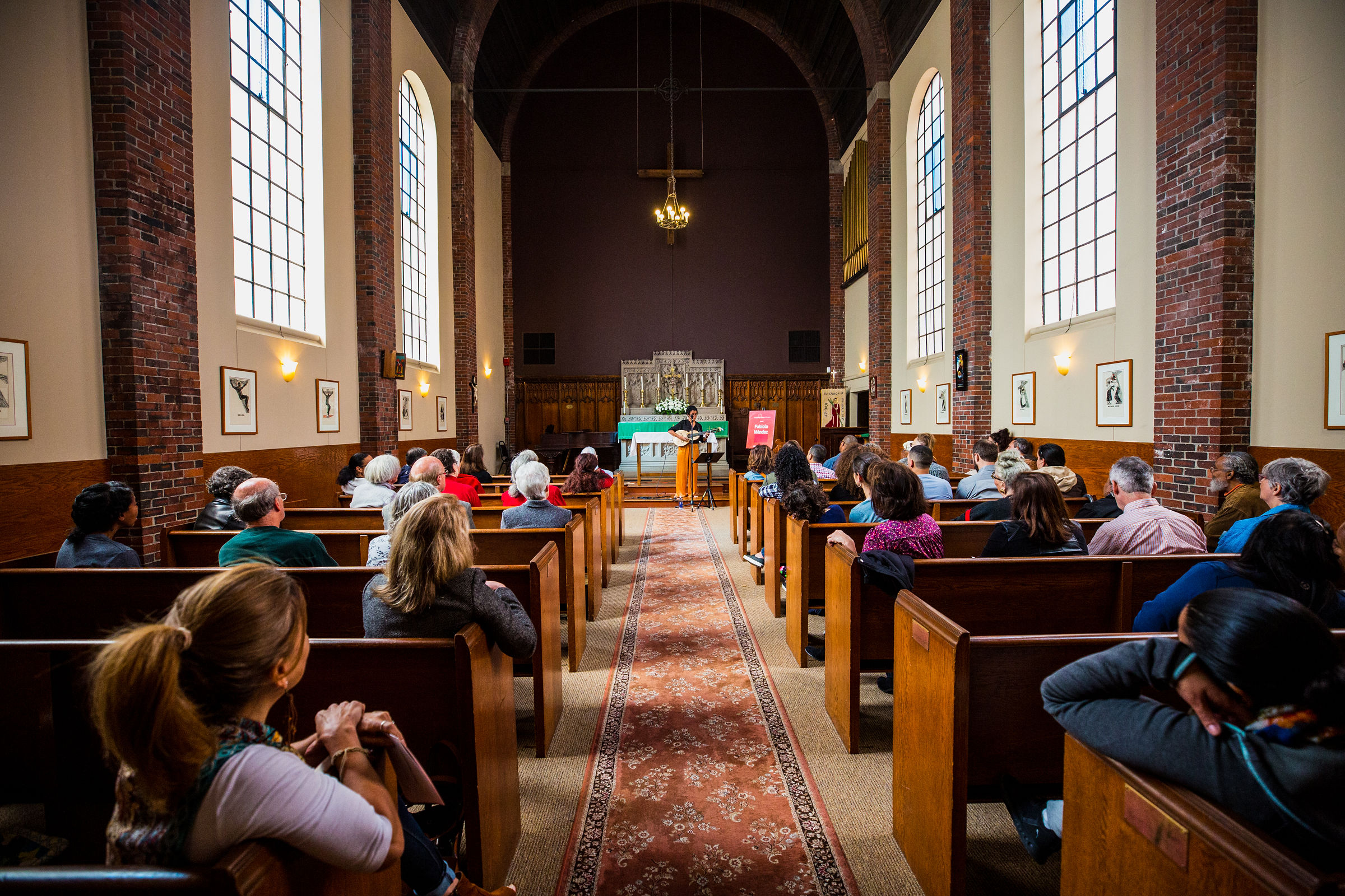 Image shows cuatrista Fabiola Méndez playing in front of a crowd, in a church in South Boston