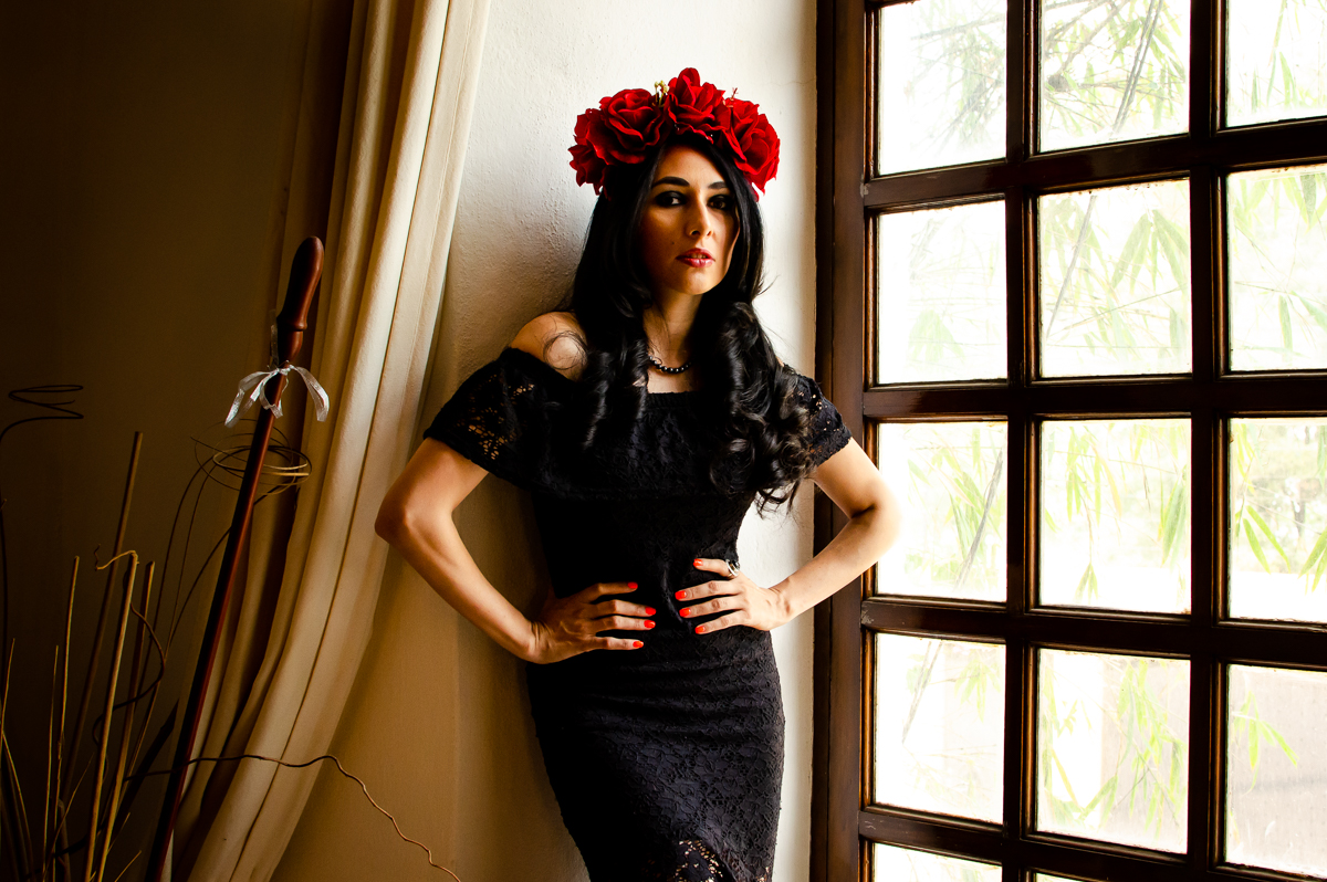 Mid-shot of a Latina women with wavy black hair, a black dress and red roses headpiece. 