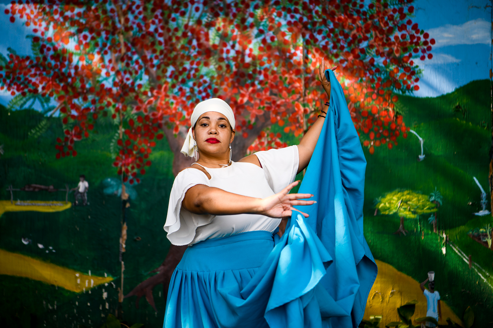 Mid-shot of Latina/Afro woman wearing traditional Bomba attire which includes, a white shirt and blue skirt and white hairwrap.