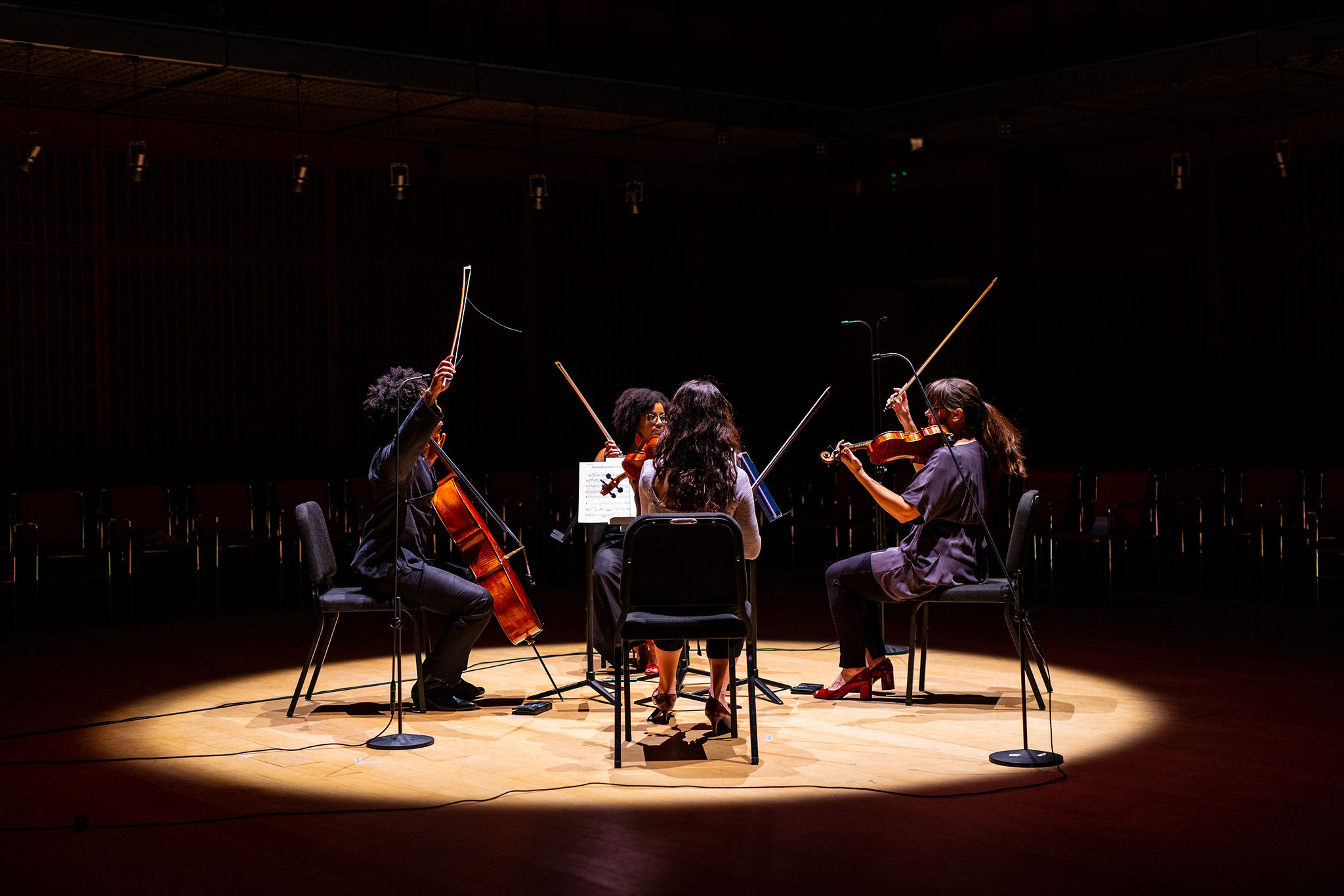 A string quartet of players facing each other in a circle, there bows proudly pointing up to the sky. 