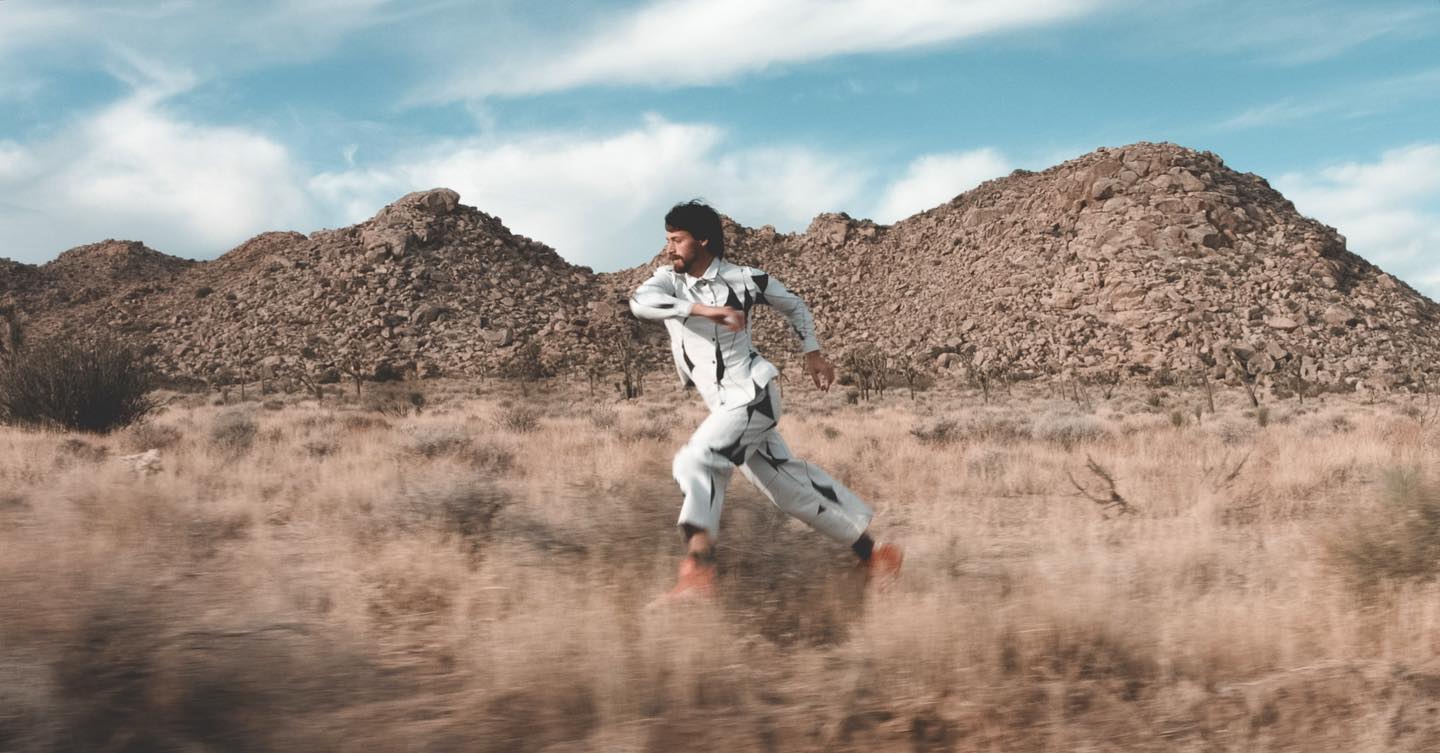 dancer Anthony Pucci runs through the mojave desert in joshua tree national park, wearing a black and white outfit with a geometric pattern and red shoes