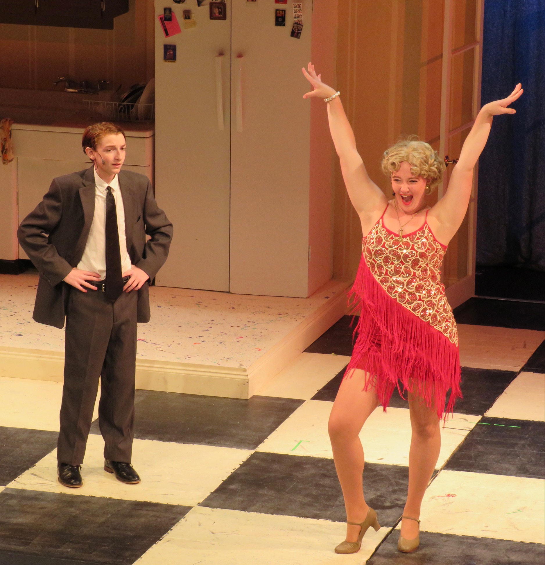 Excited performer in a red fringe dress exclaiming with her arms up, performer on left side looking displeased at the excited dancer