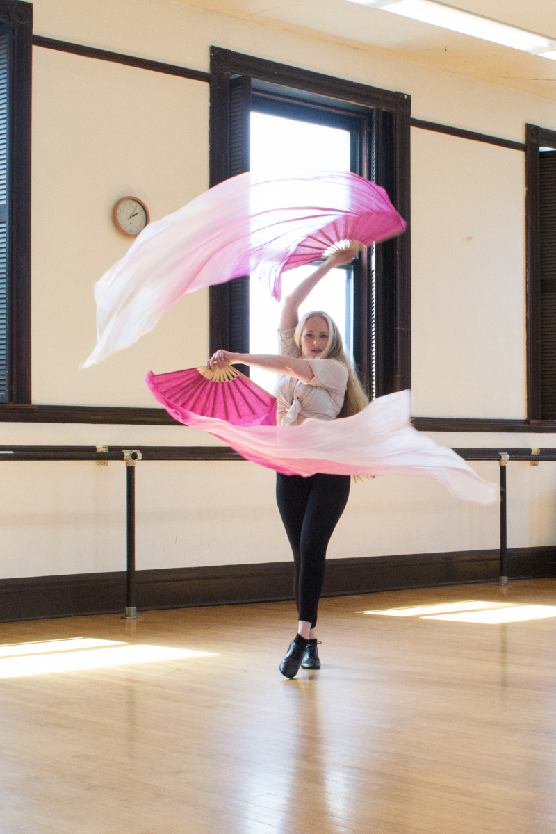 A woman dancing with fans that trail long silk veils in ombre pinks
