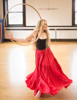 A woman with long red hair dancing with a hula hoop, and wearing a long full bright red skirt.