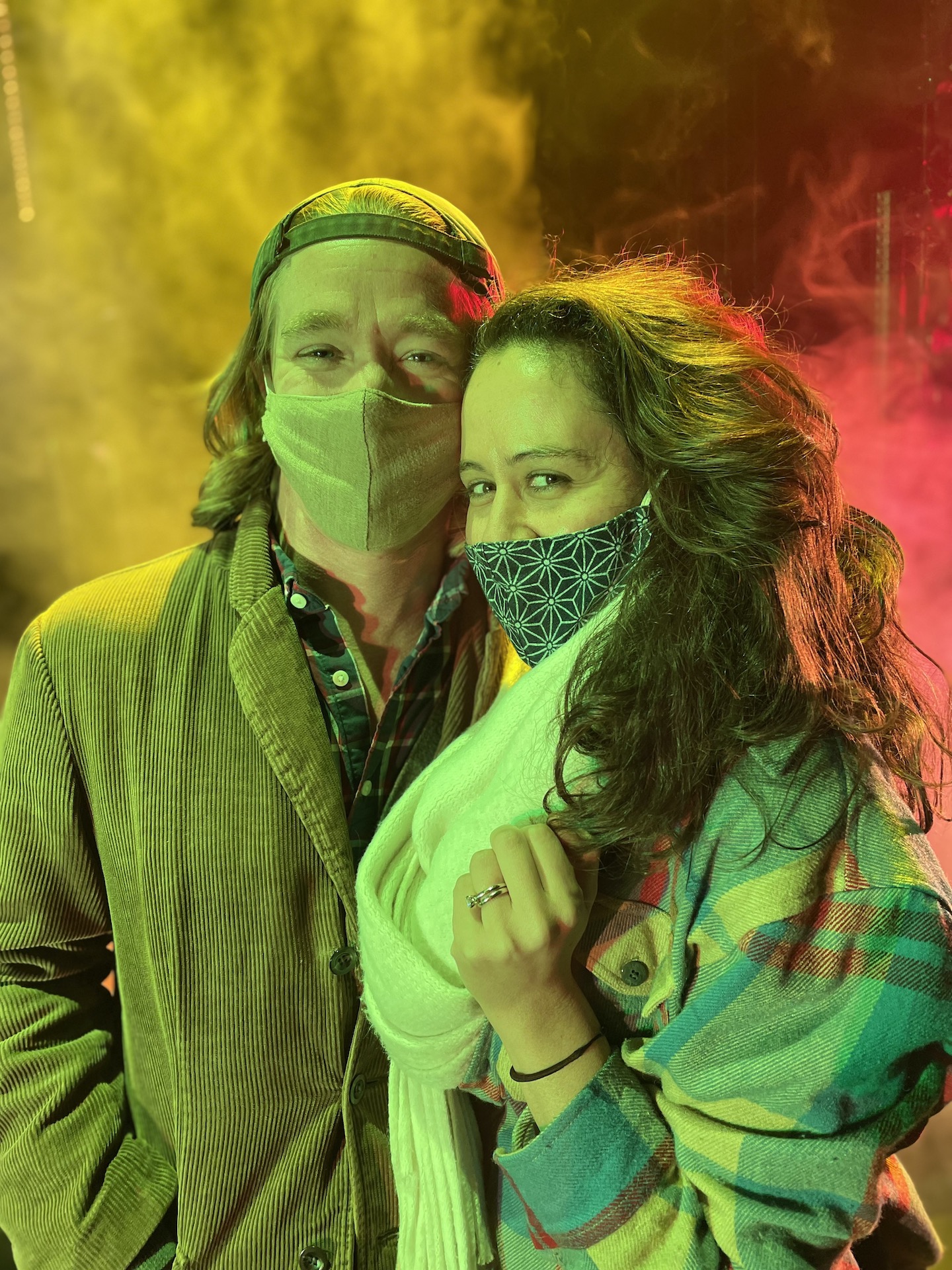Tyler and artistic partner Taibi pose at a production of MacBeth in Stride - two smiling, masked faces in front of colorful smoke - with vibes like a rock show as theater