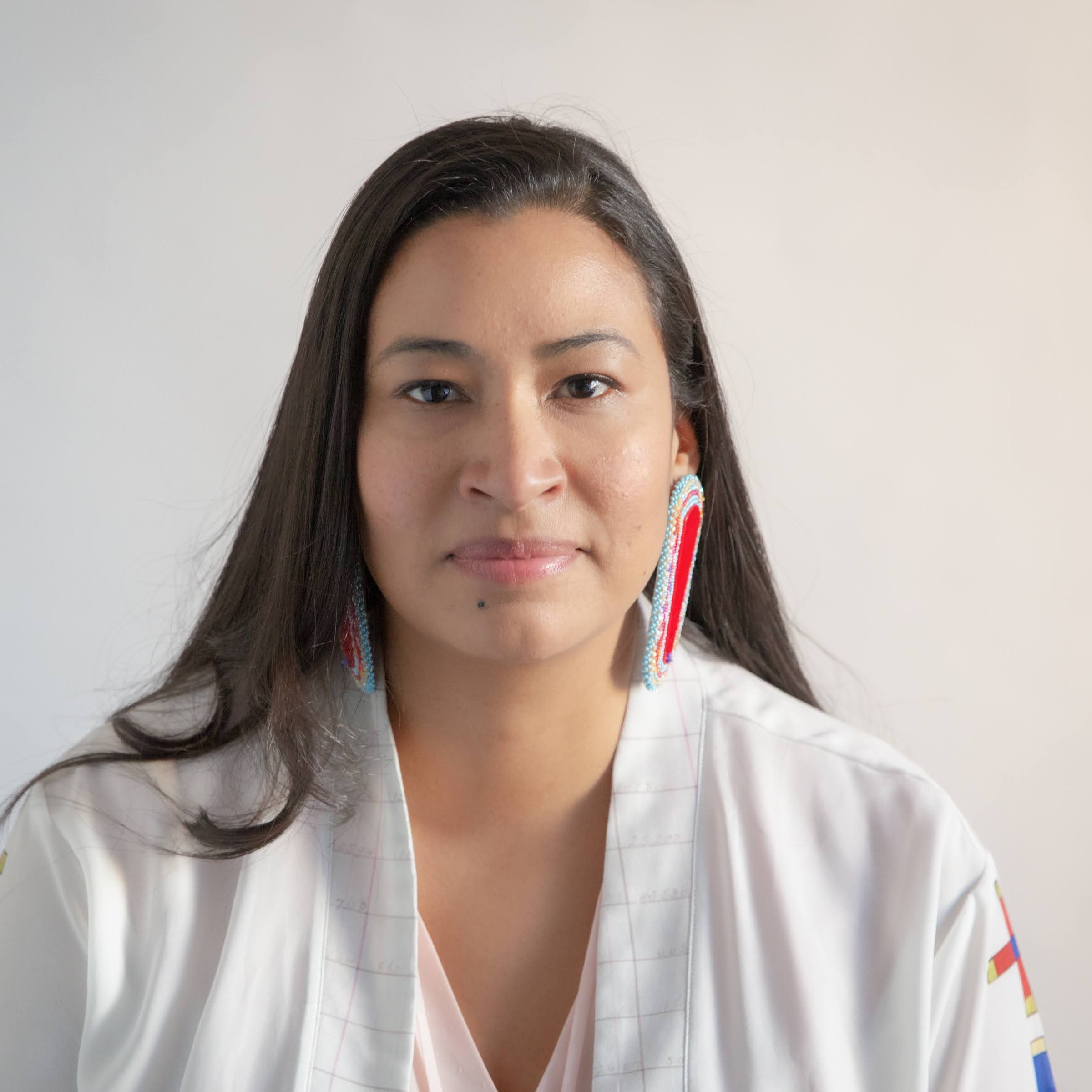 Headshot of Silvermoon, Dark brown hair, black eyes, brown skin, wearing a white shirt and large red beaded earrings with a multicolor trim