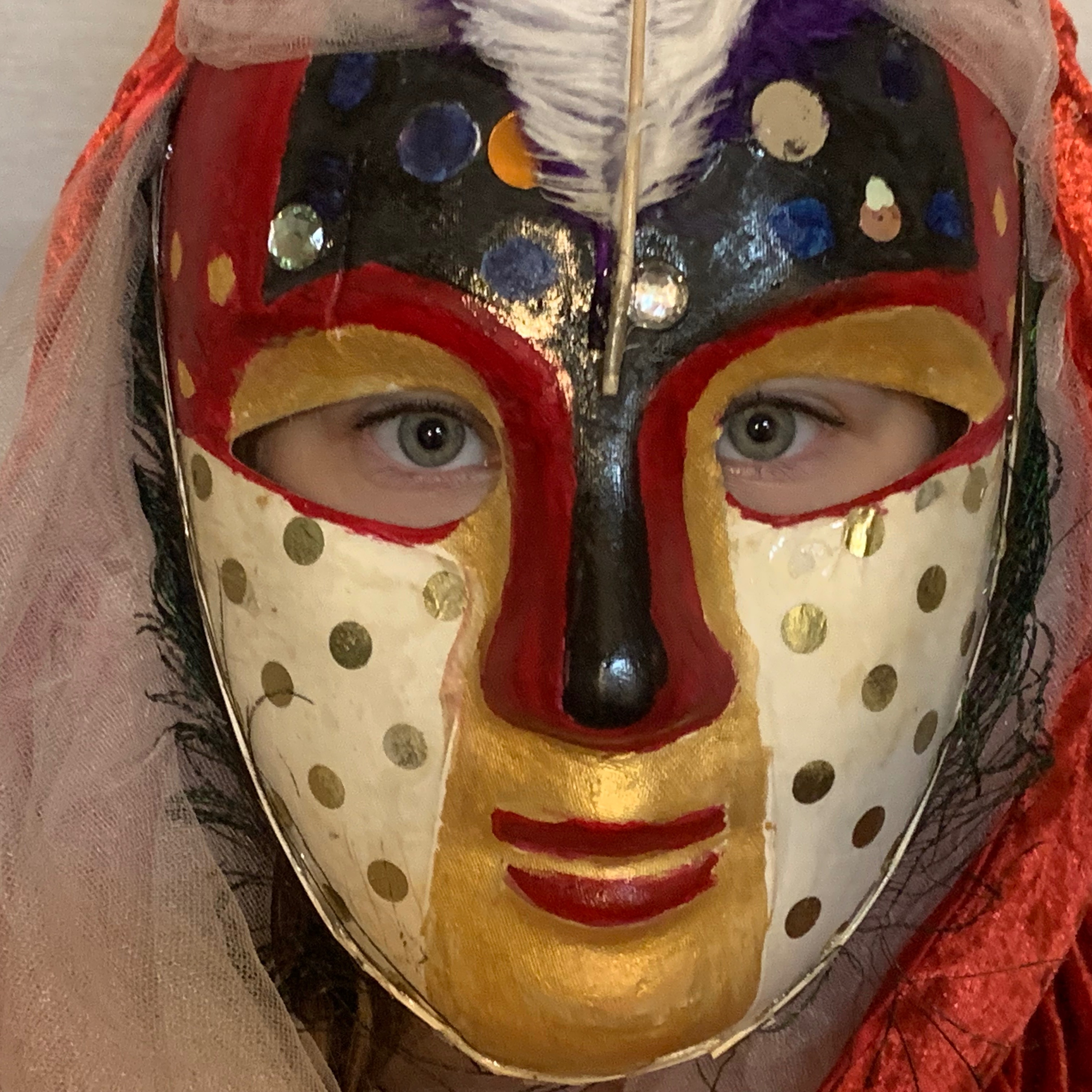 Eyes looking out of Image of full mask- red and black contrasted with gold-white pattern