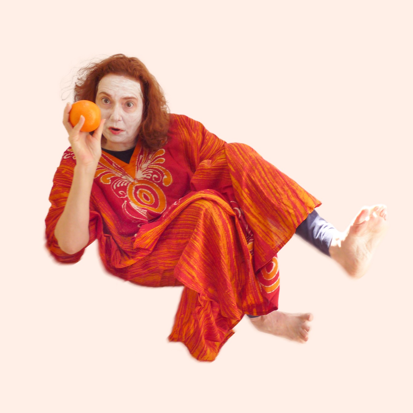 Jean Minuchin in white clown face with a bright orange robe floating in an pale orange background staring at an orange.
