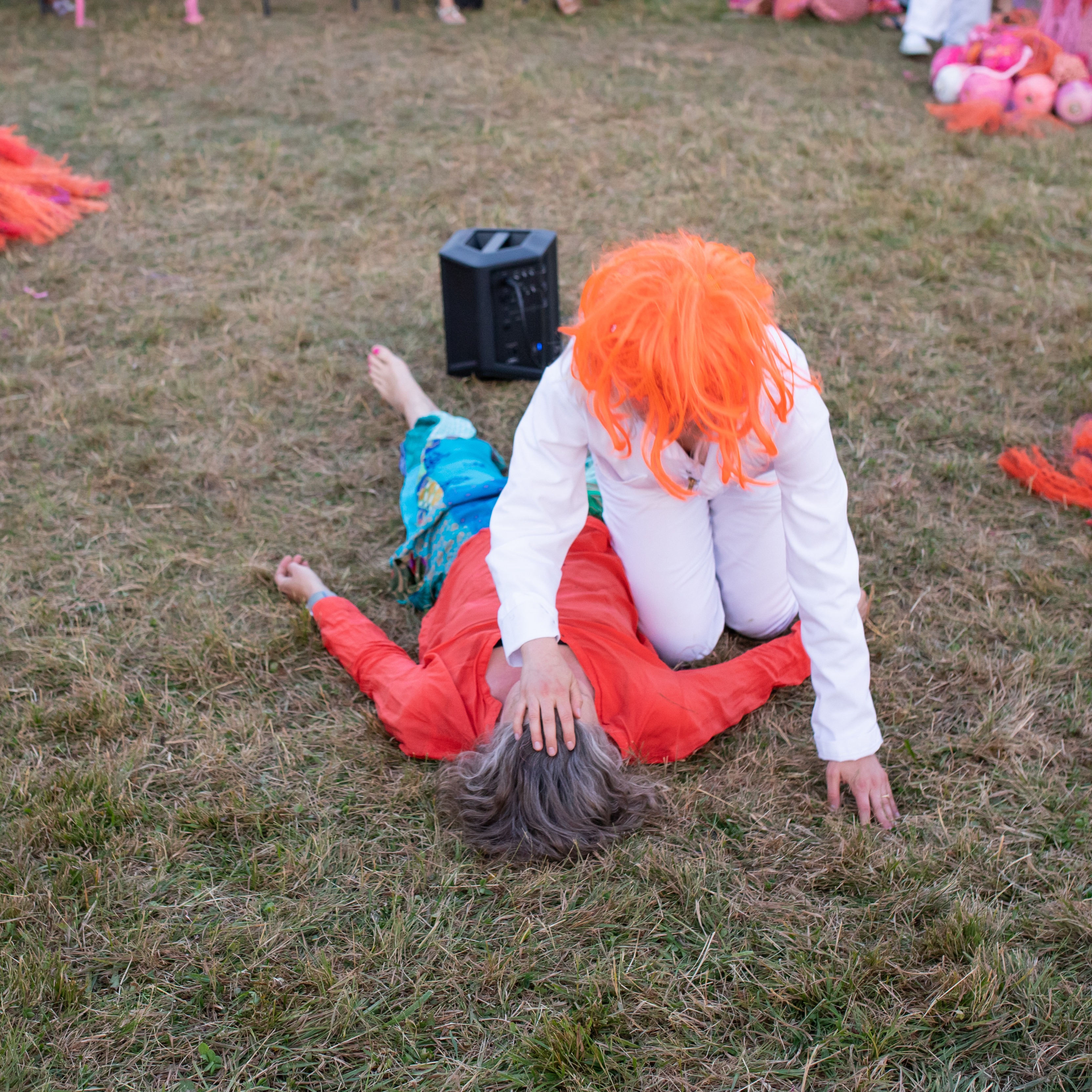 Hannah, wearing an orange wig, performs a fake healing on an audience member by touching her head