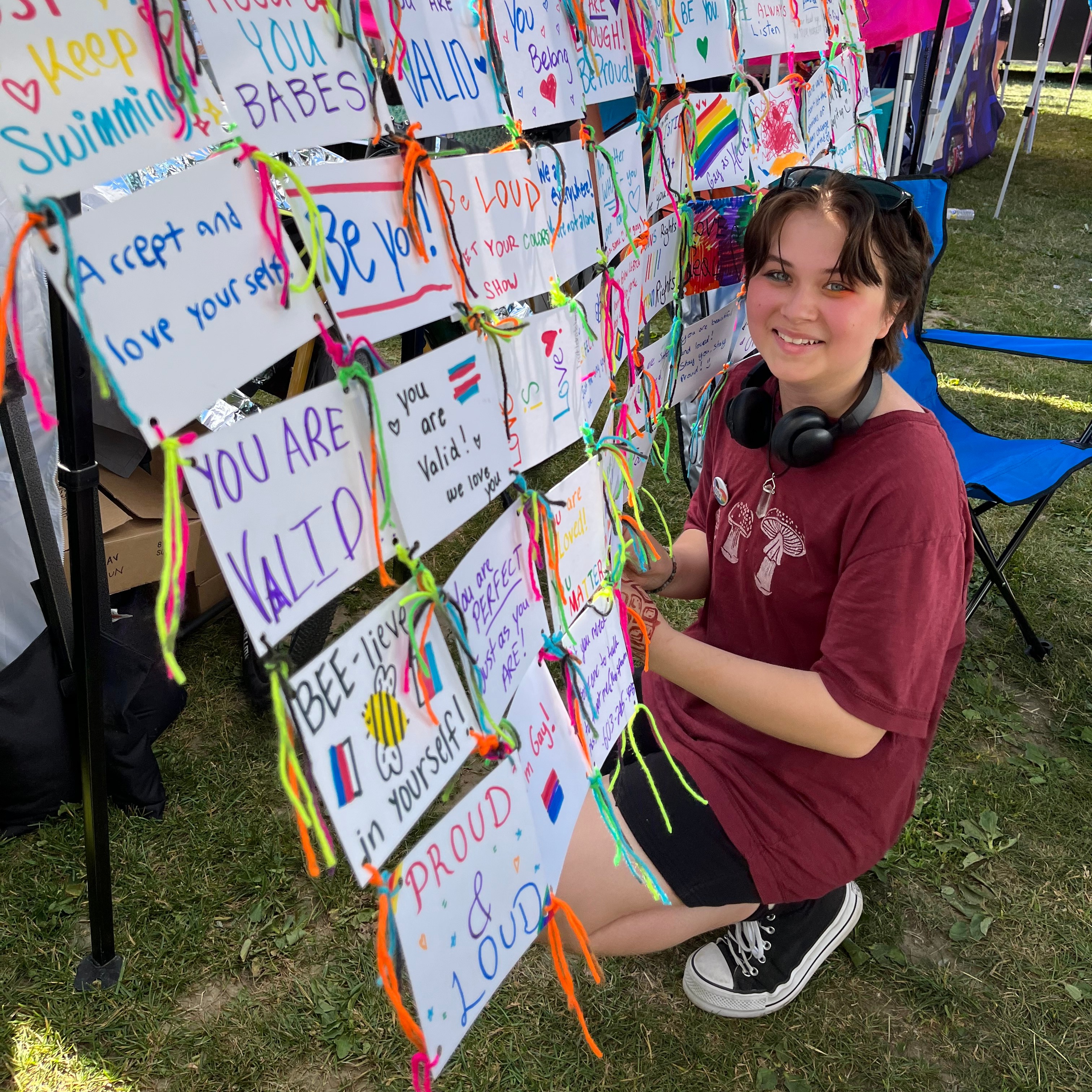 With a cheerful expression, a teenager looks directly at the camera while skillfully attaching a string to a handcrafted arrangement of paper, resembling a "quilt."
