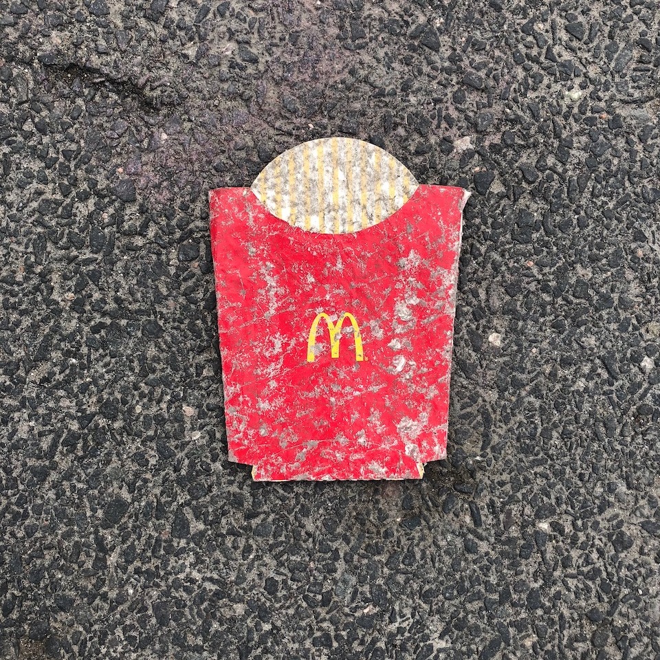 An image of a McDonald's french fry holder that has been littered and flattened into pavement