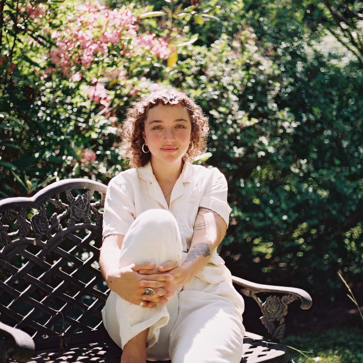 A woman dressed in all white with curly hair sitting in a garden.
