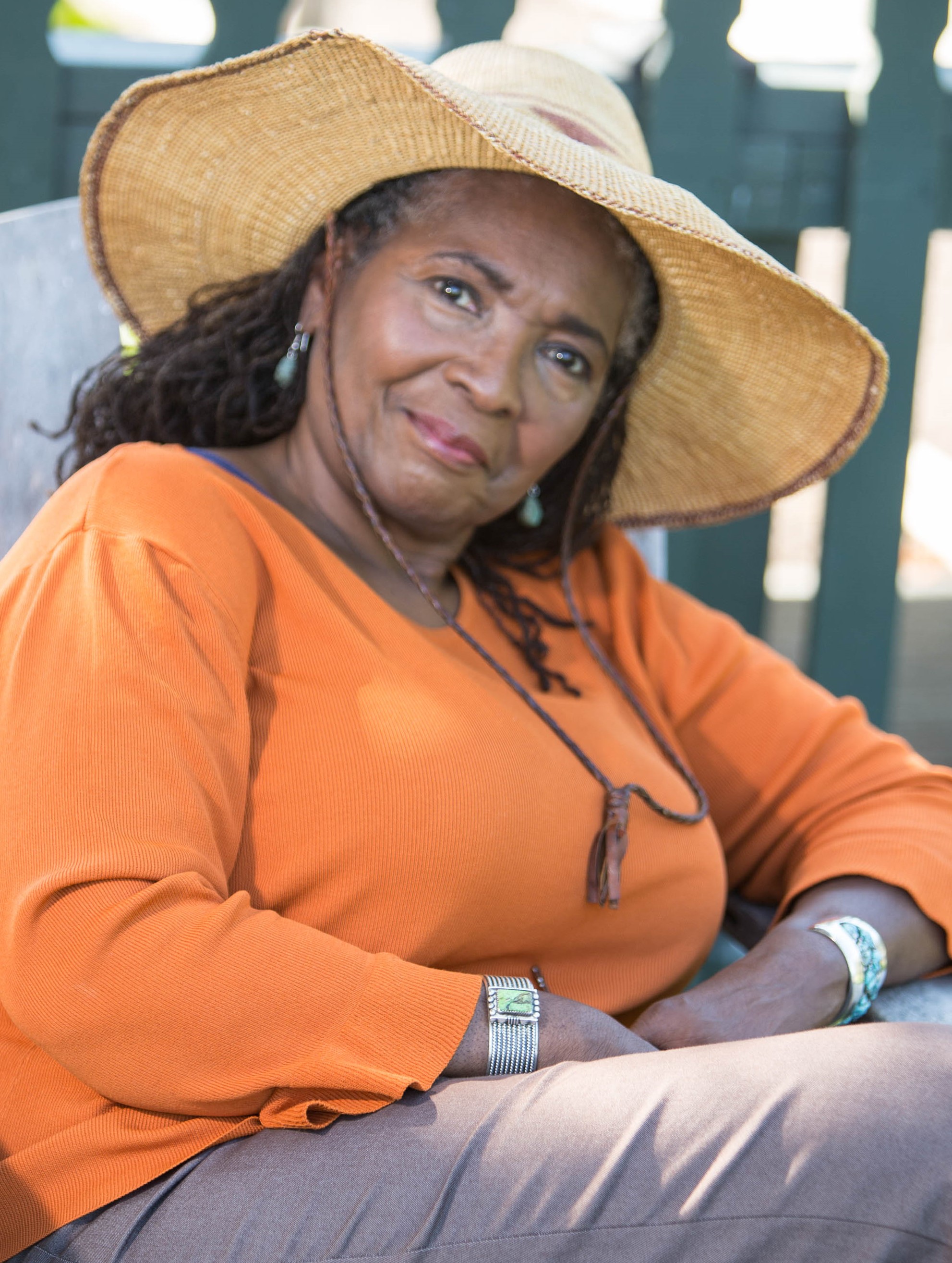 Black woman wearing a sun hat and orange sweatshirt smiling at the camera
