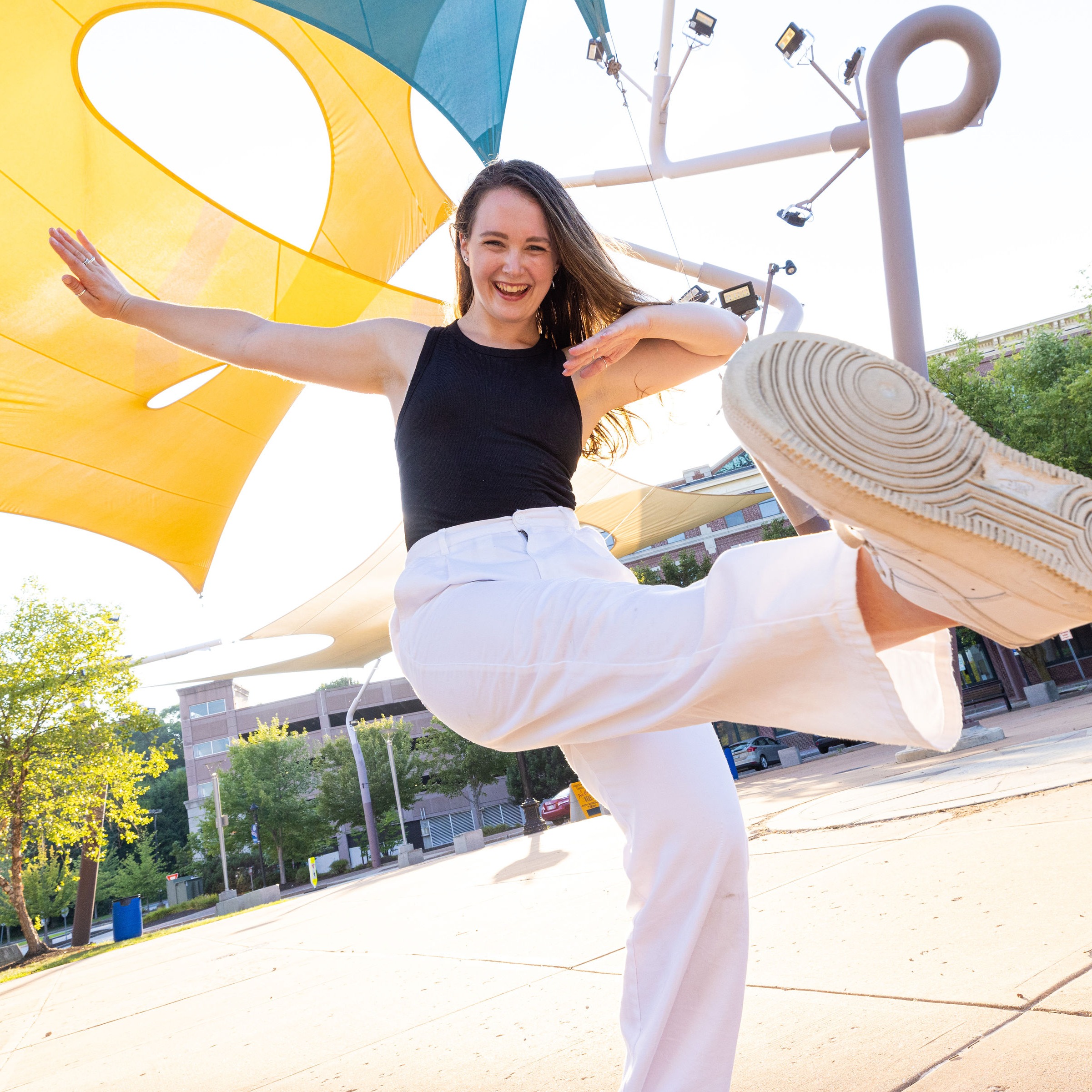 Dancer in a black top and white pants smiling in a pose