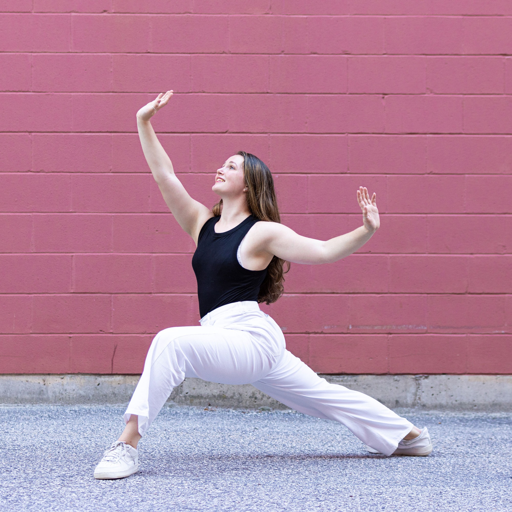 Dancer in white pants and black top in a lunge looking out and up