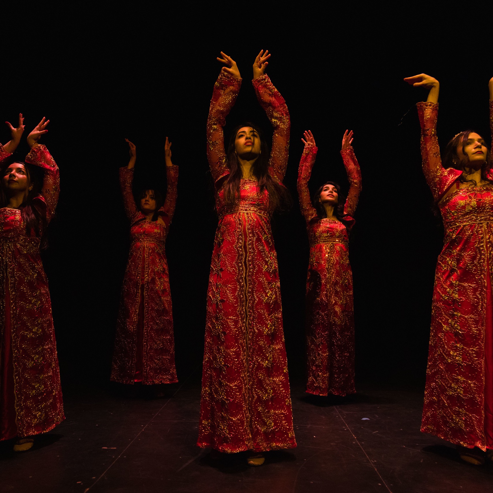 A group of women in long red dresses with their arms lifted in the air.