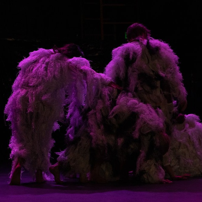 A group of performers are in fuzzy suits, becoming a blob of humans