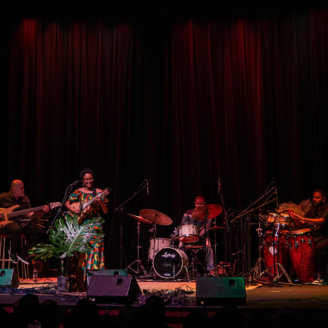 Image shows Fabiola Méndez and her quartet on stage: cuatro/vocals, bass, congas, and drummer