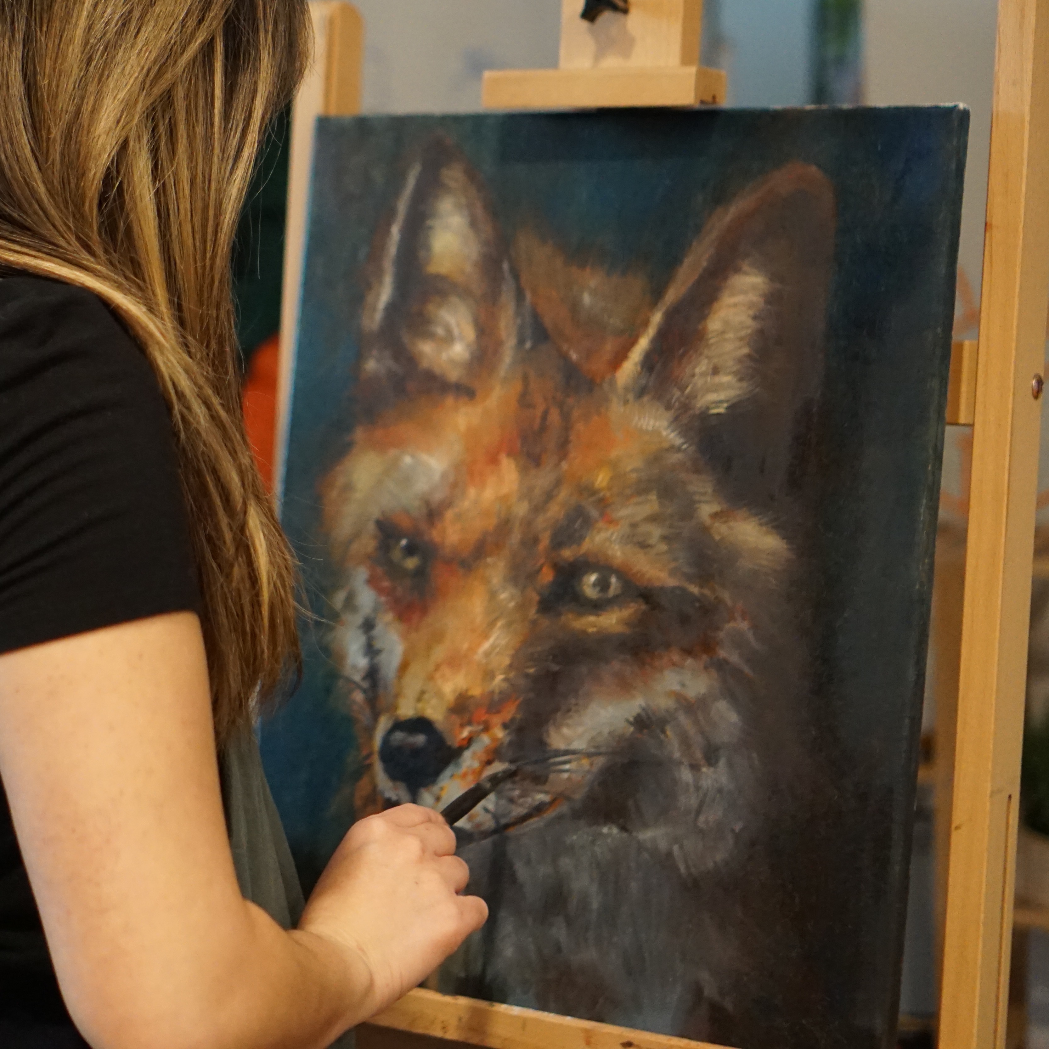 Erica at her easel painting a colorful fox with oil paint.