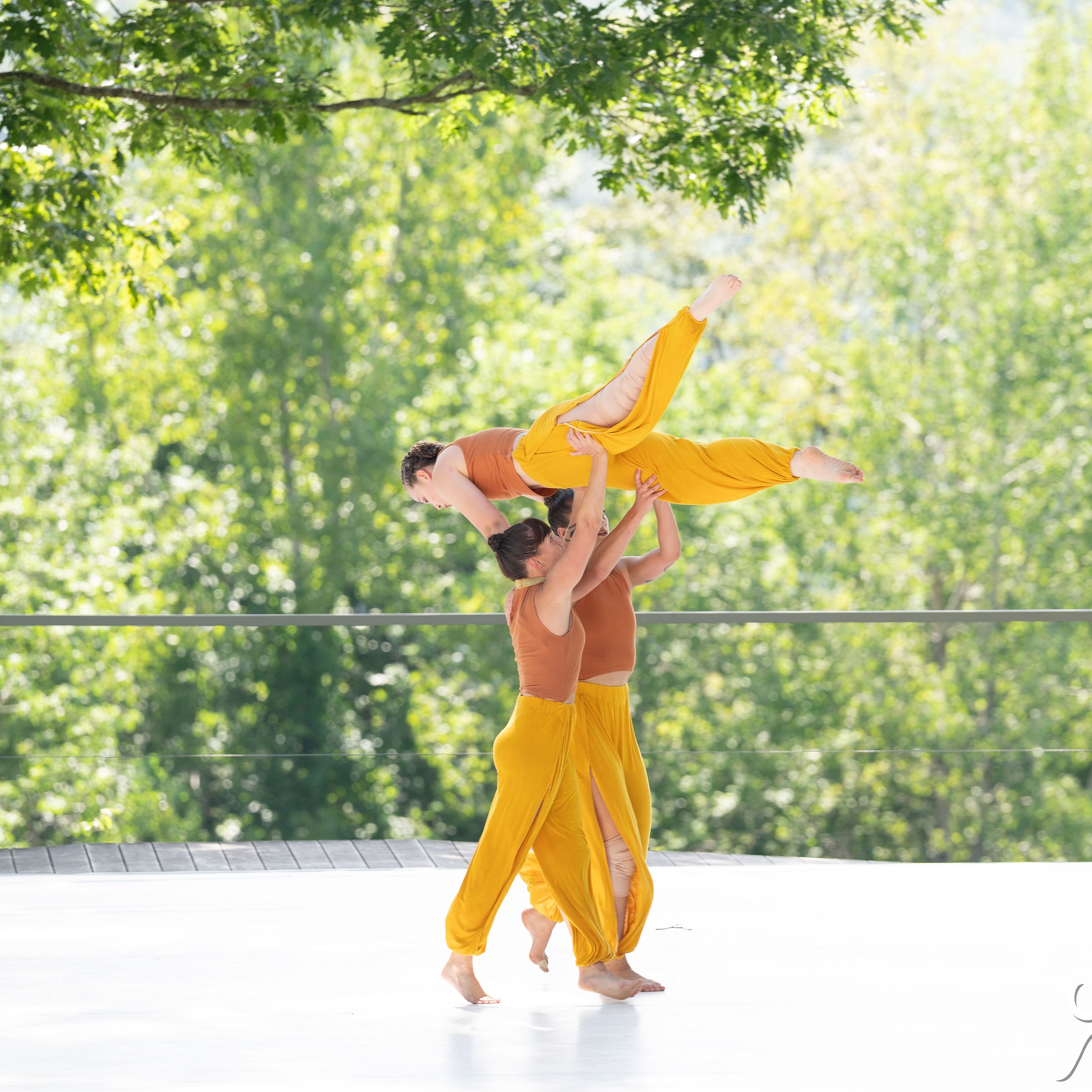 Two female dancers lifting another dancer over their heads in a super woman flying position with gorgeous trees in the background