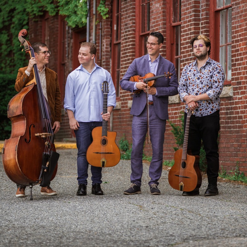 Outdoor photo of the 4 band members standing with their instruments: upright bass, guitar, fiddle, and guitar