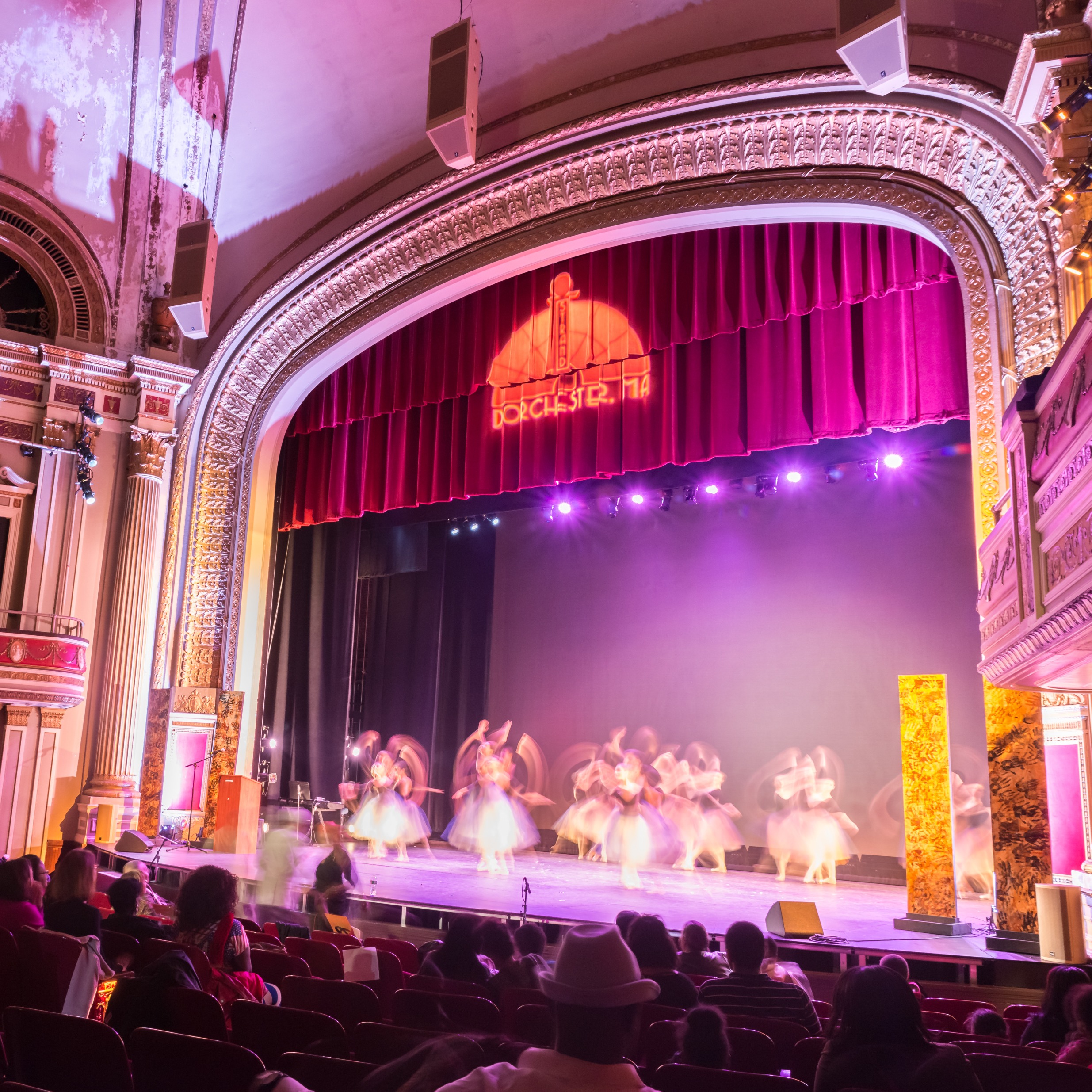 A performance of twirling Ballerinas happens on stage while an audience looks on within the historic interior of the Strand Theatre in Dorchester.
