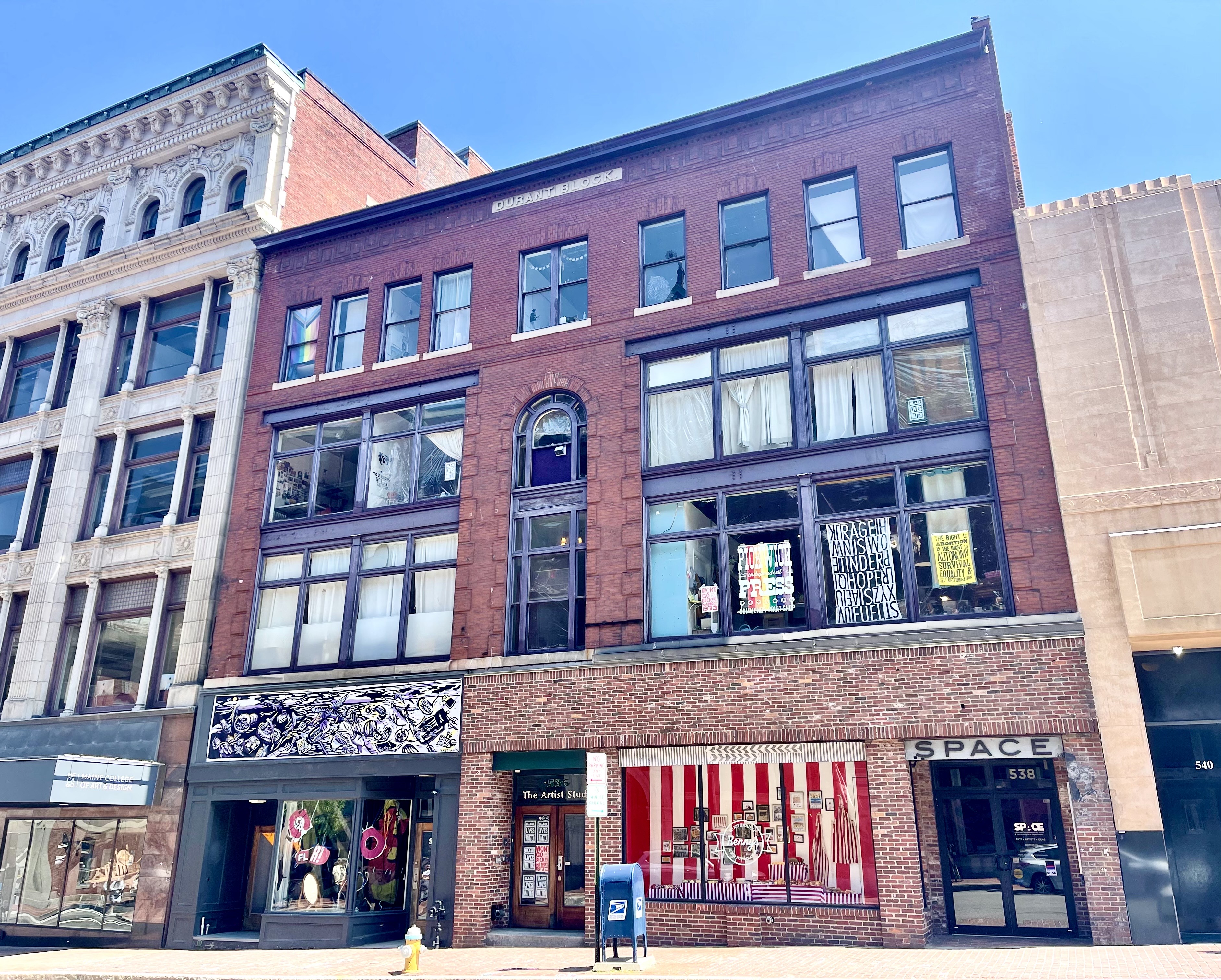 a photograph of SPACE Gallery on Congress Street in spring 2023 shows a vibrant window exhibit between the primary exhibition space and main venue