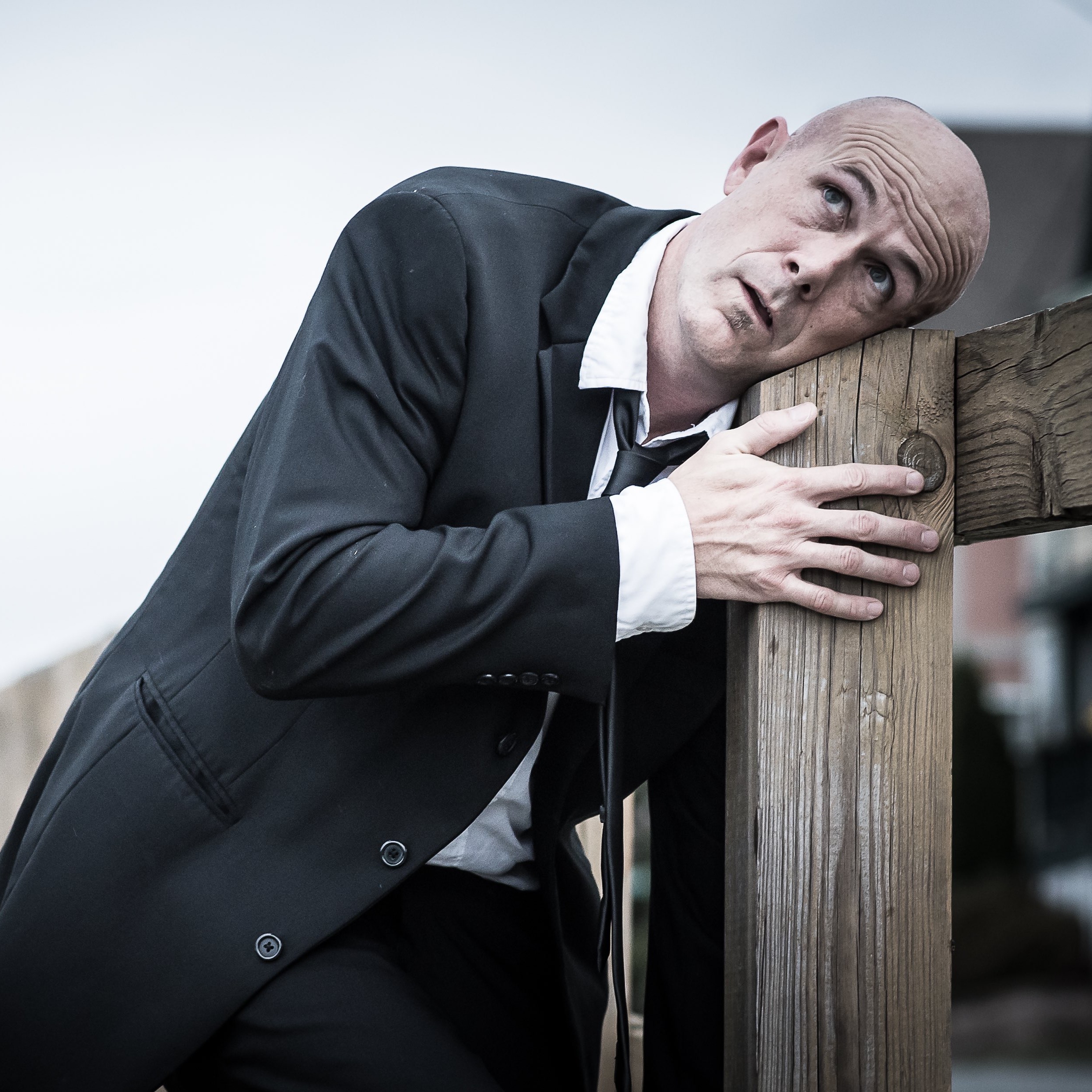 man in suit leans head on fence post