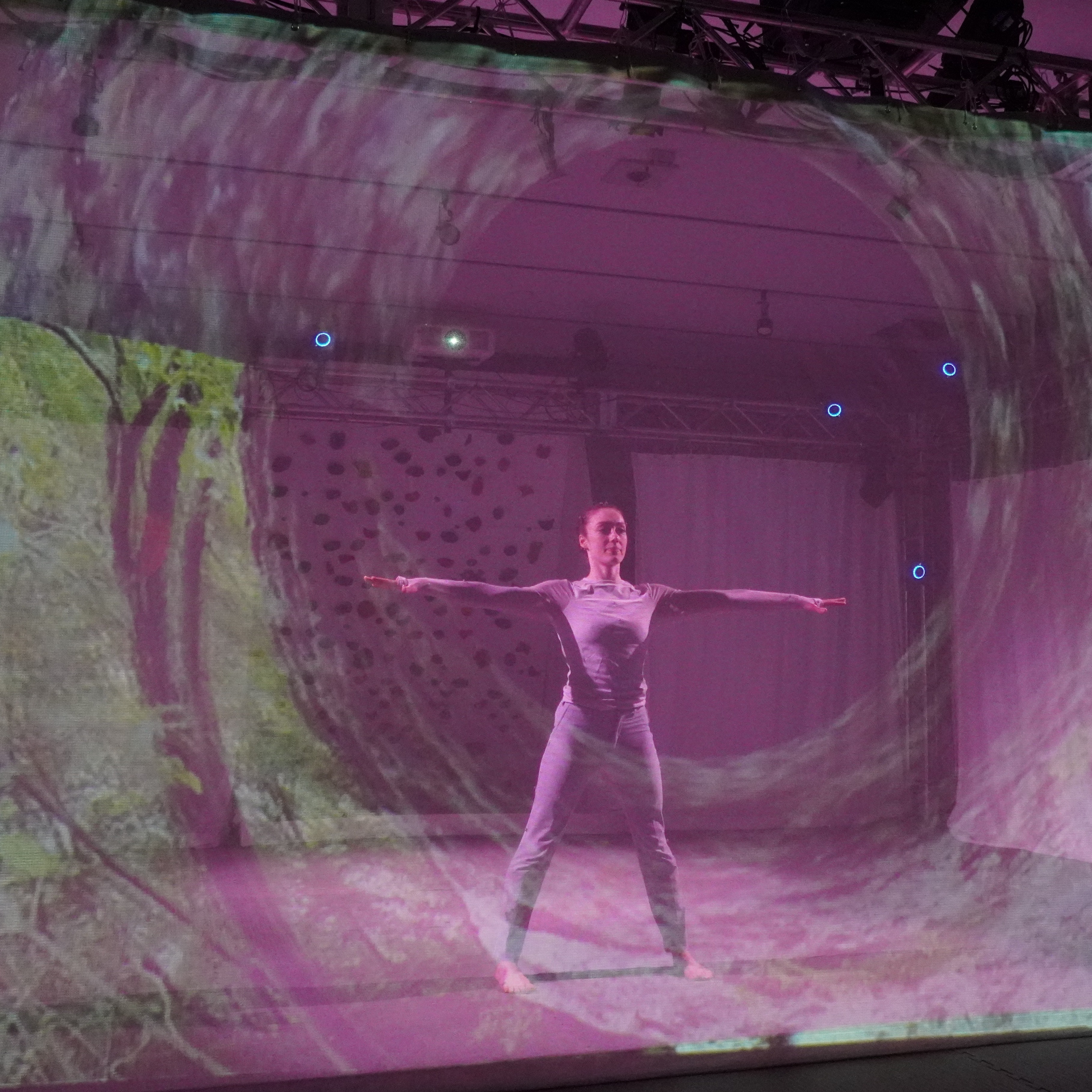 Ellen is standing with her arms out to the side. She is positioned behind a scrim, with images of outdoor climbing projected.