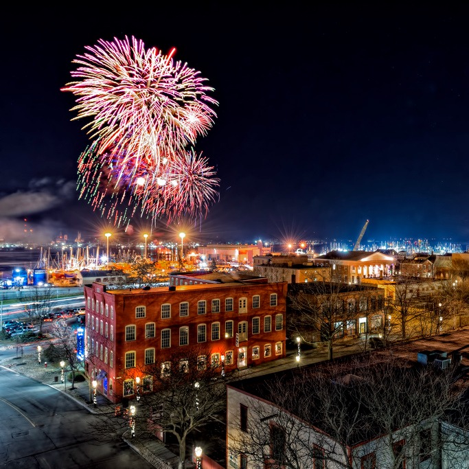 Night time image taken from rooftop of downtown New Bedford facing east with fireworks exploding in the sky.