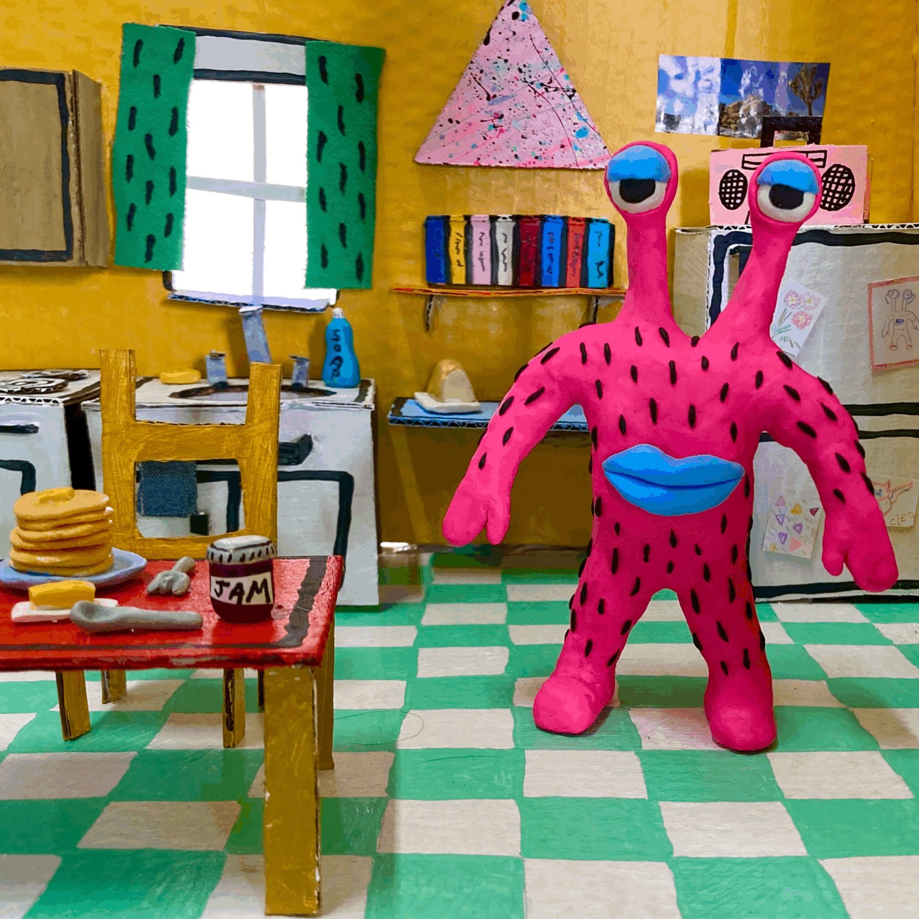 Miniature stop-motion set of a colorful cardboard kitchen with a pink clay monster inside of it