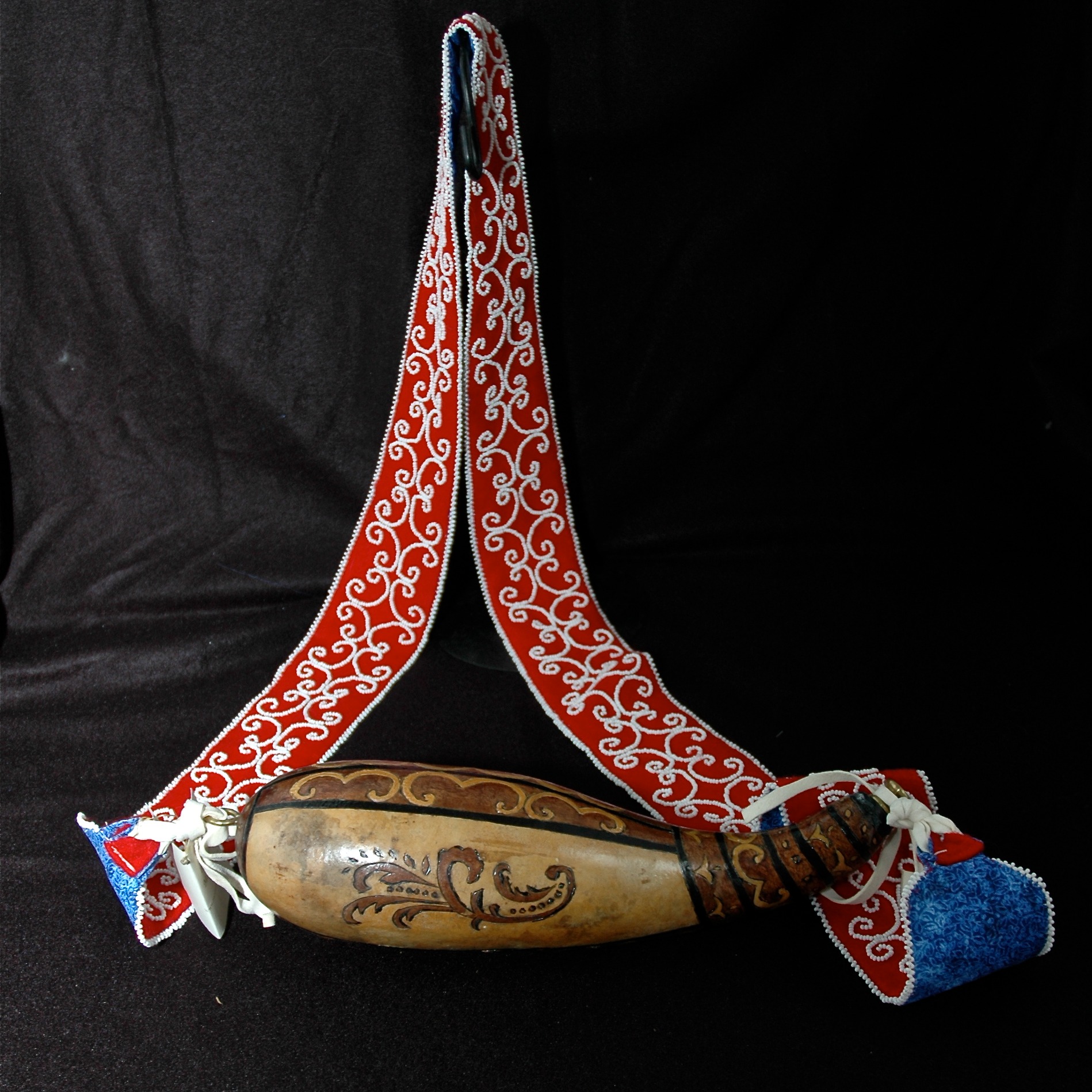 Gourd Powder Horn decorated with tribal designs.  Strap is red wool backed by blue calico cotton.  White seed beads are used to create double curves and edging along the strap.