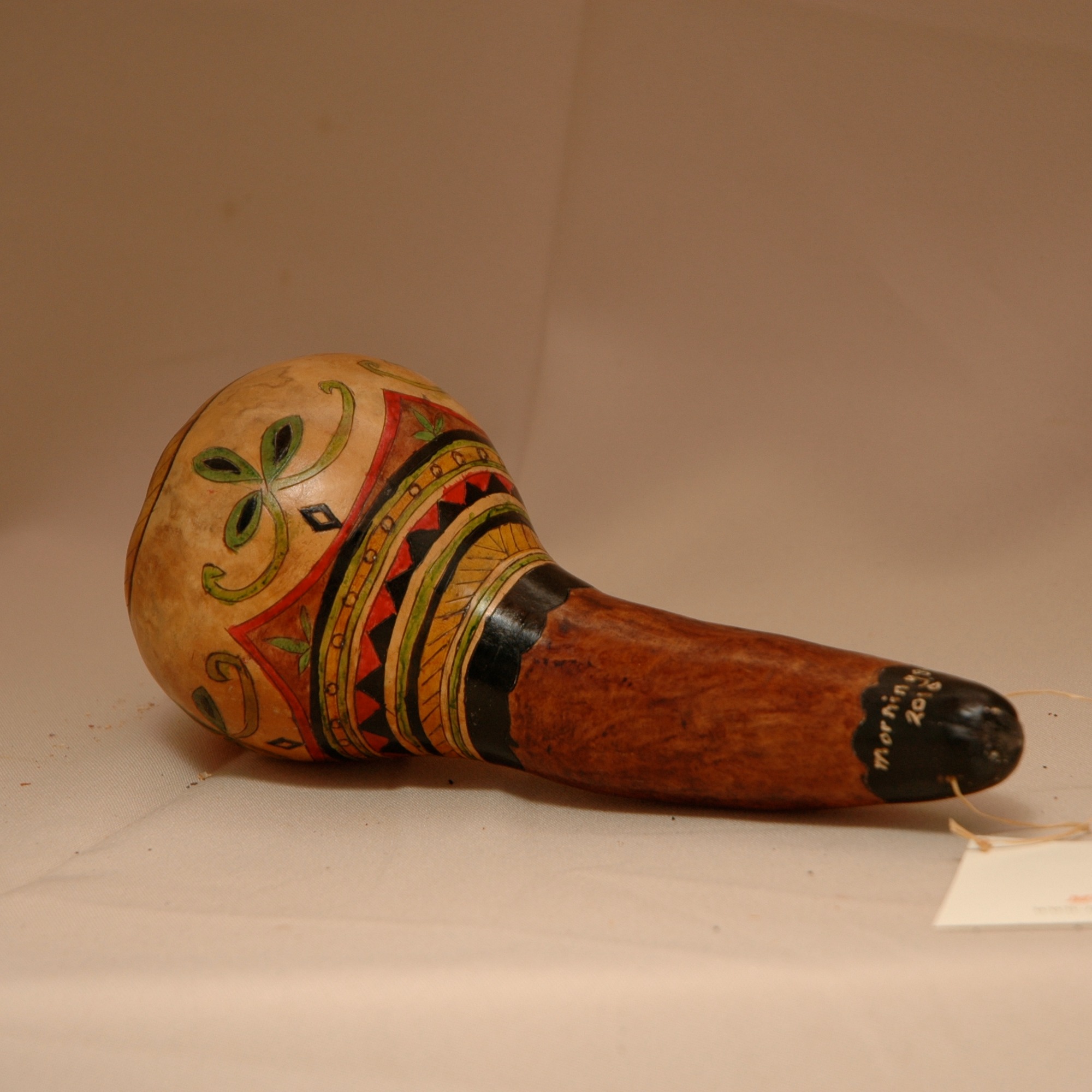 Gourd Rattle is approximately seven inches in length and has a five inch bulb. Tribal designs ring the rattle.