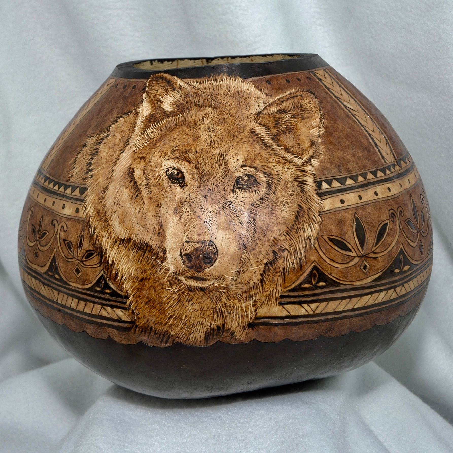 Woodburned gourd bowl features head of wolf on front and full running wolf on the back.  Ringed with various tribal designs.