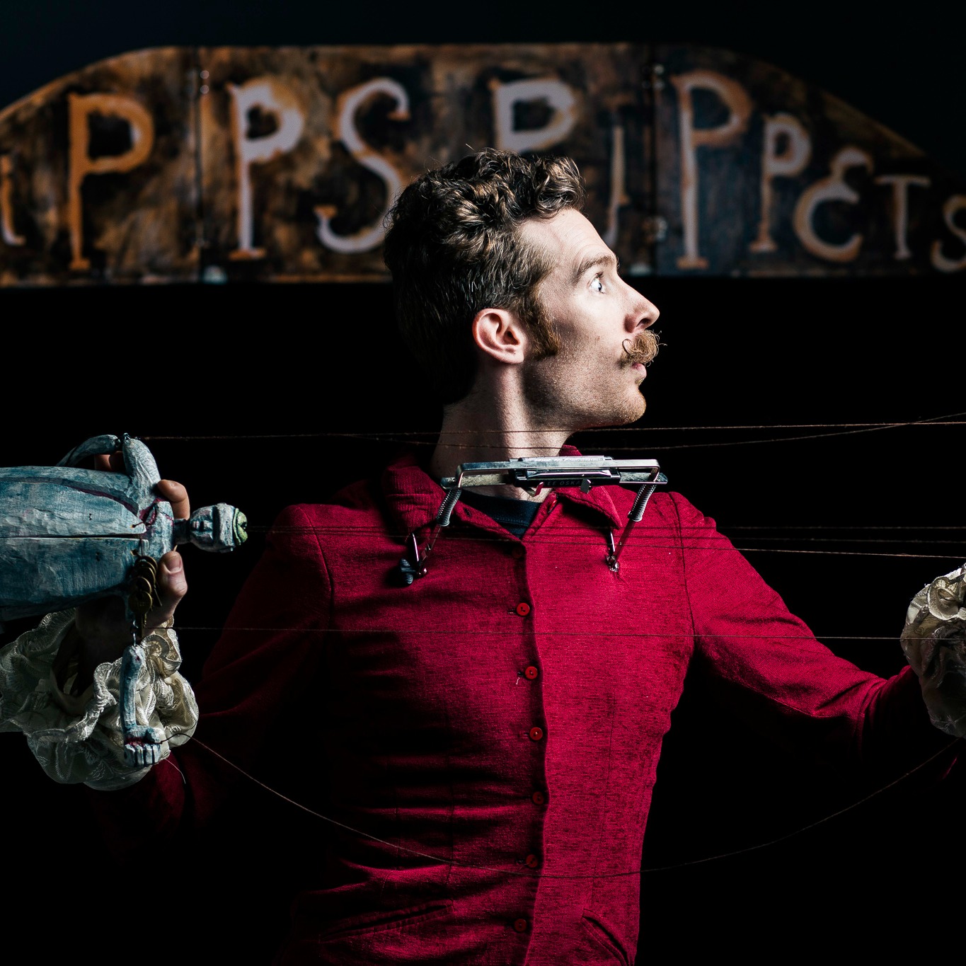 Madison J. Cripps mustacioed and laden with neck holster harmonica in the key E minor holding the wooden marionette Flip who is blue with a tiny bowler hat and a big belly