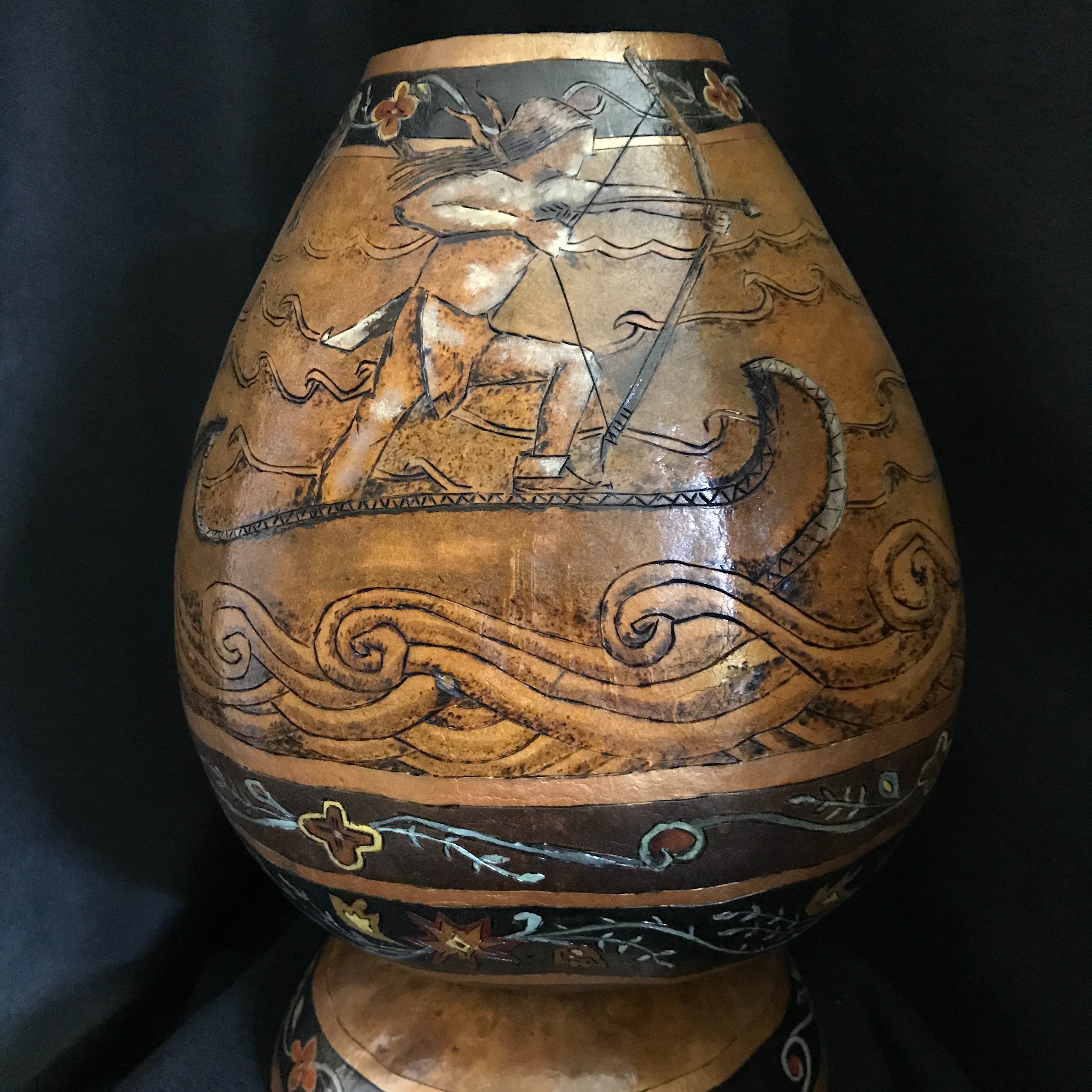 Story gourd tells the story of Gluskap fighting the water serpent and how woodpecter got his red head.  Illustration circles entire gourd. Has a gourd base. Woodburned and colored.r