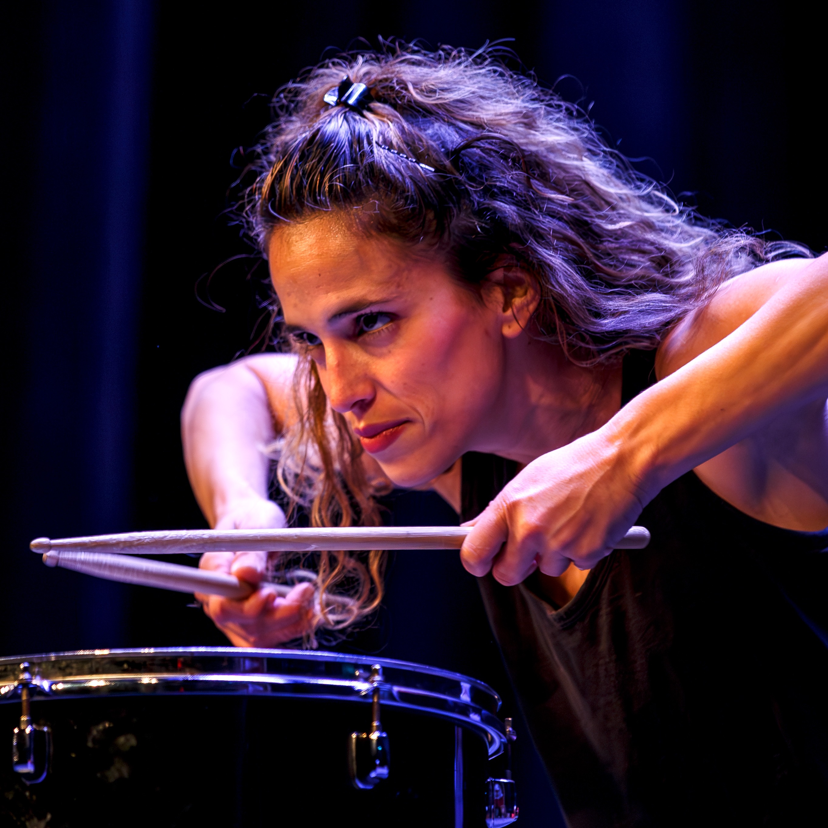 Female drummer holding drumsticks above a drums, looking intensely into the audience