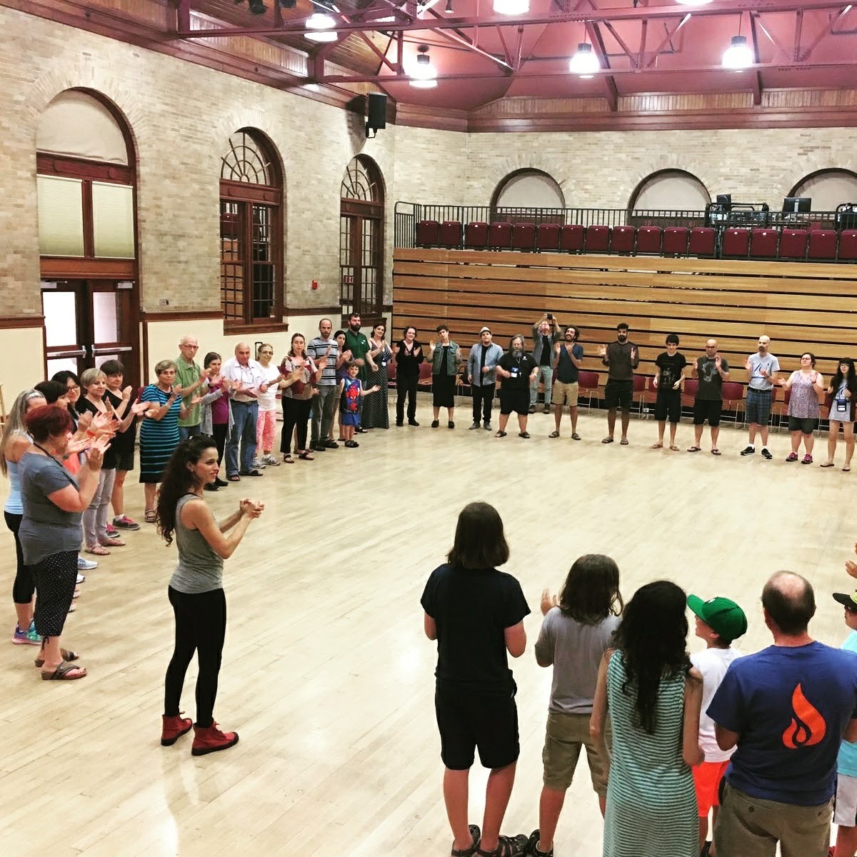 A large group of people standing in a circle, following a leader with clapping.