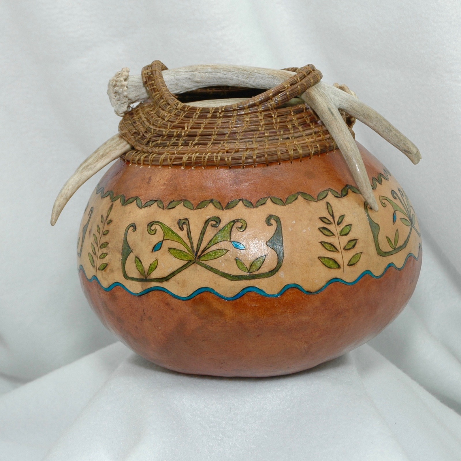 Gourd bowl topped with white taile deer antler and pine needle coiling.  Accented with tribal designs include the ash tree.